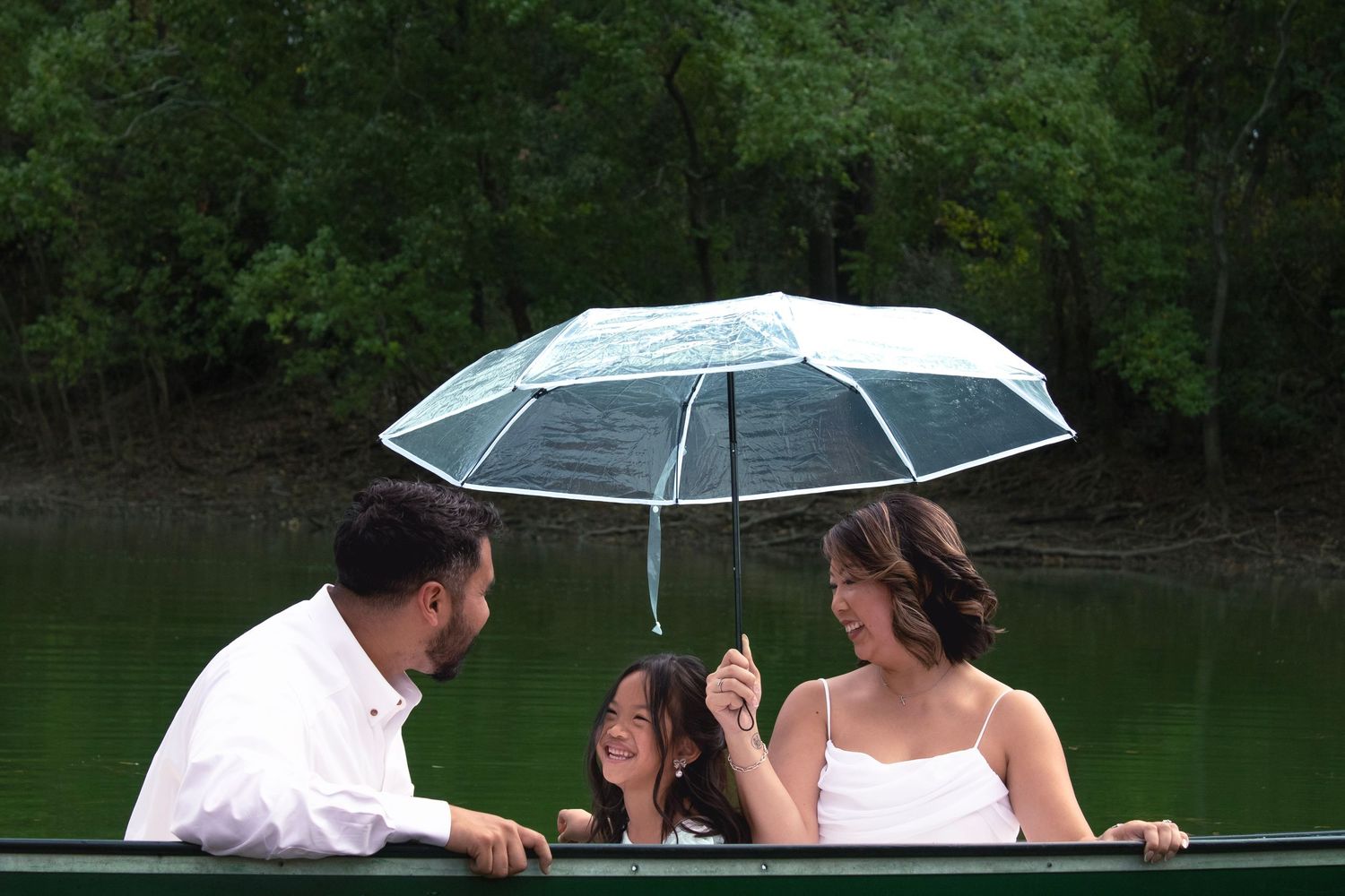 Couple shares romantic moments under clear umbrella while rowing on tranquil lake.