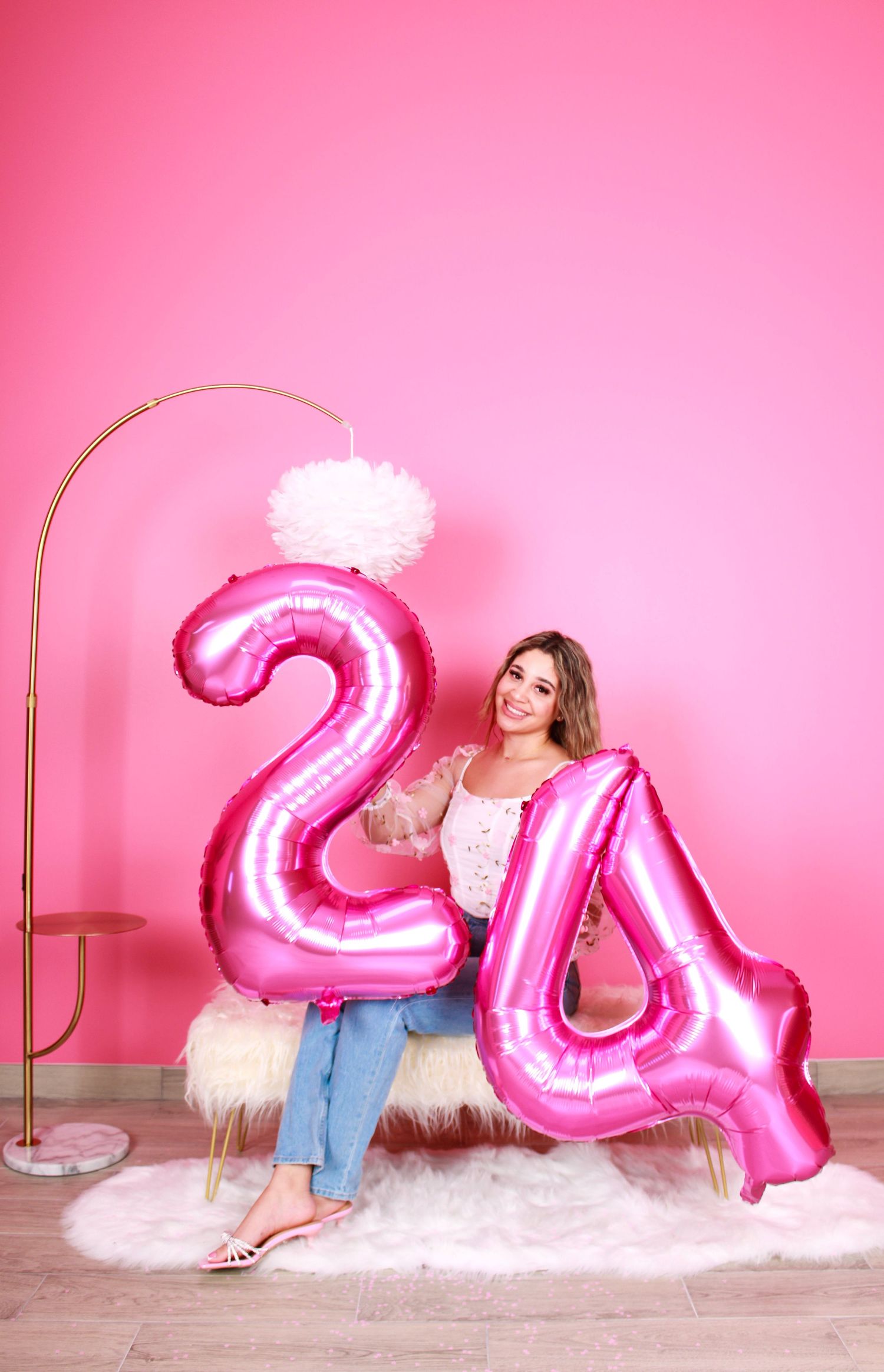 Large pink number balloons displayed on white fluffy rug against pink wall.