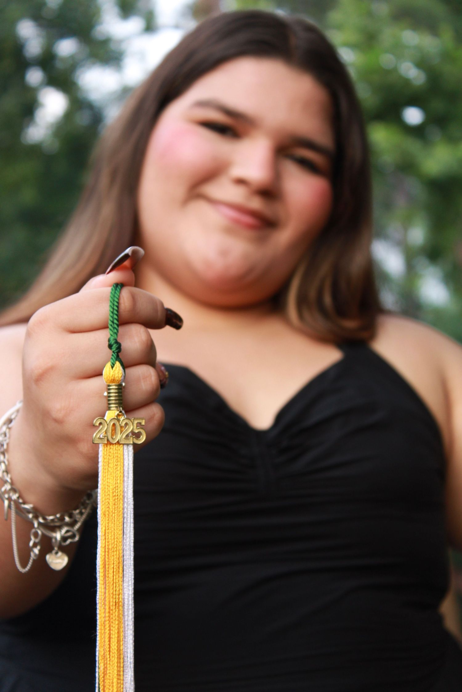 Graduate holding yellow tassel with 2023 charm in black dress.