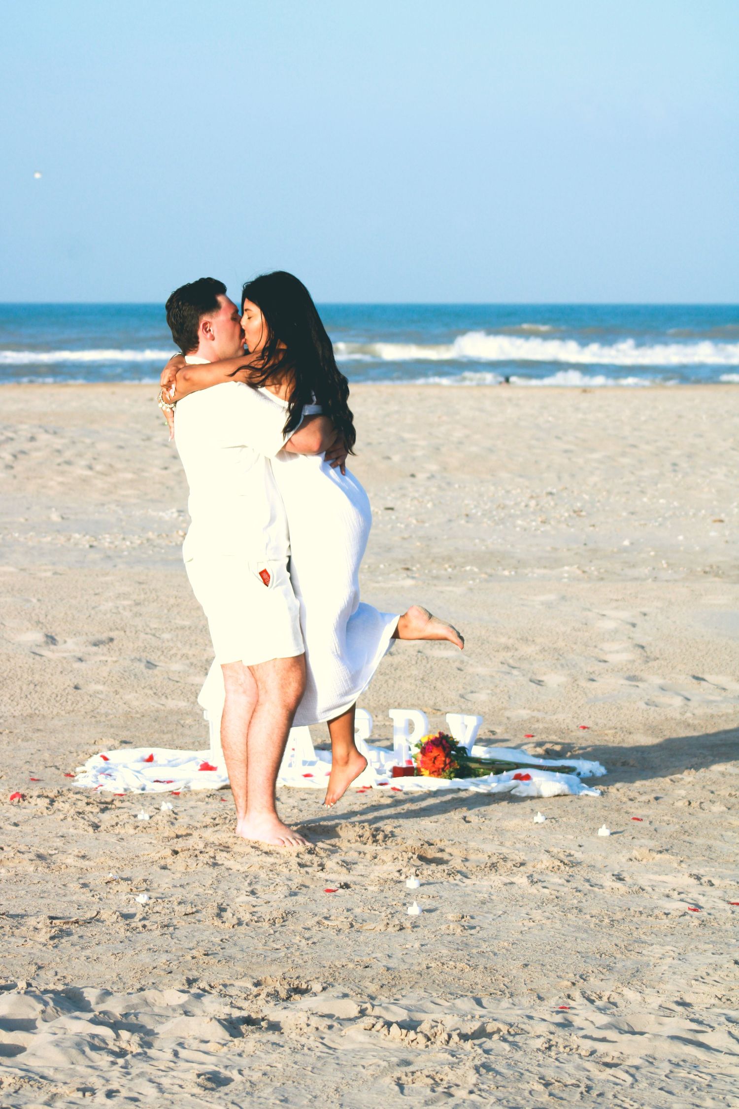 Romantic beach proposal with couple embracing by the ocean.