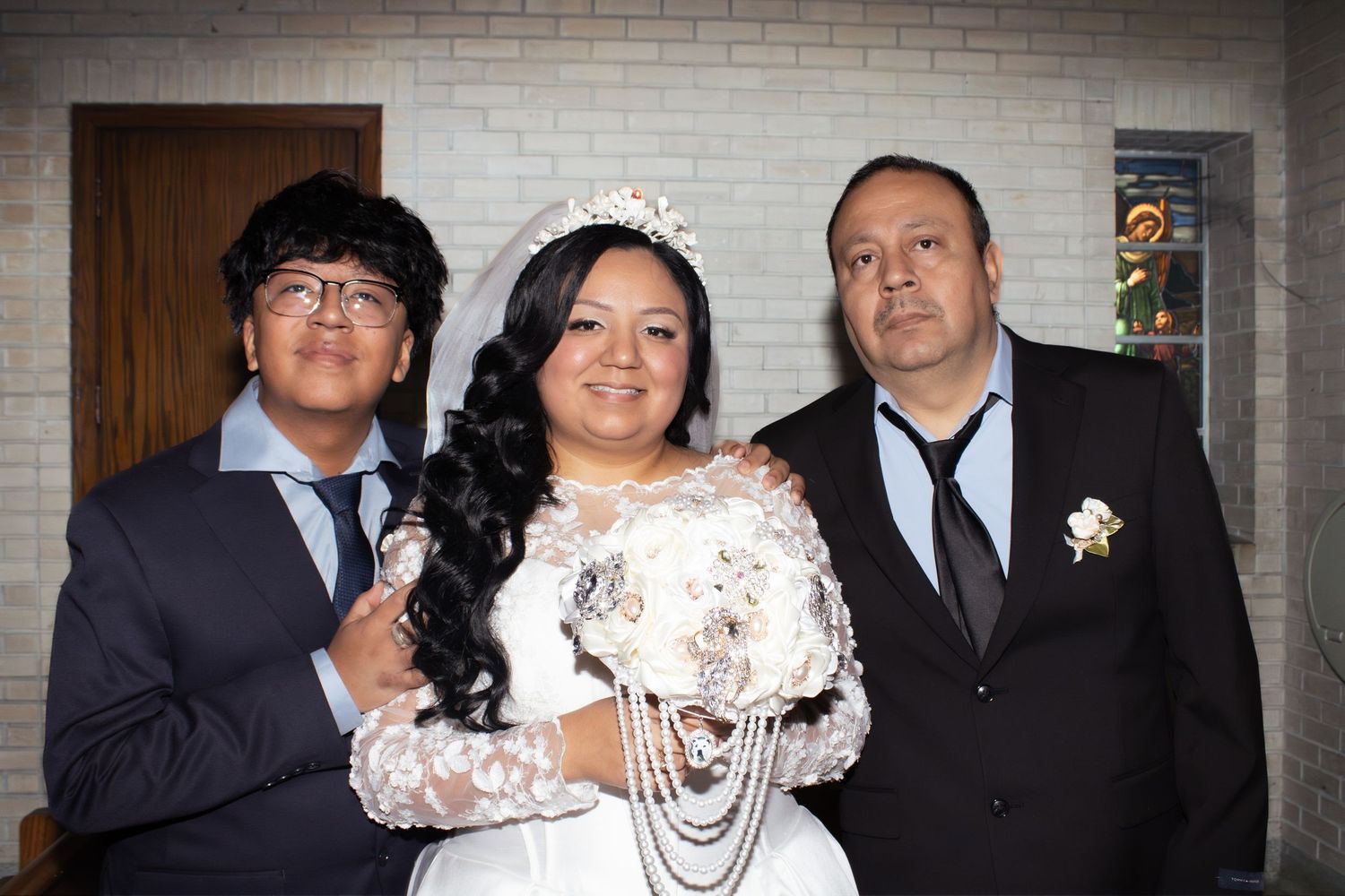 Wedding party members in formal attire posing against brick wall background.