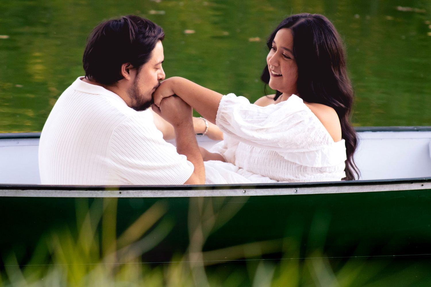 A couple in white clothing sharing romantic moments in a rowboat on a peaceful lake.