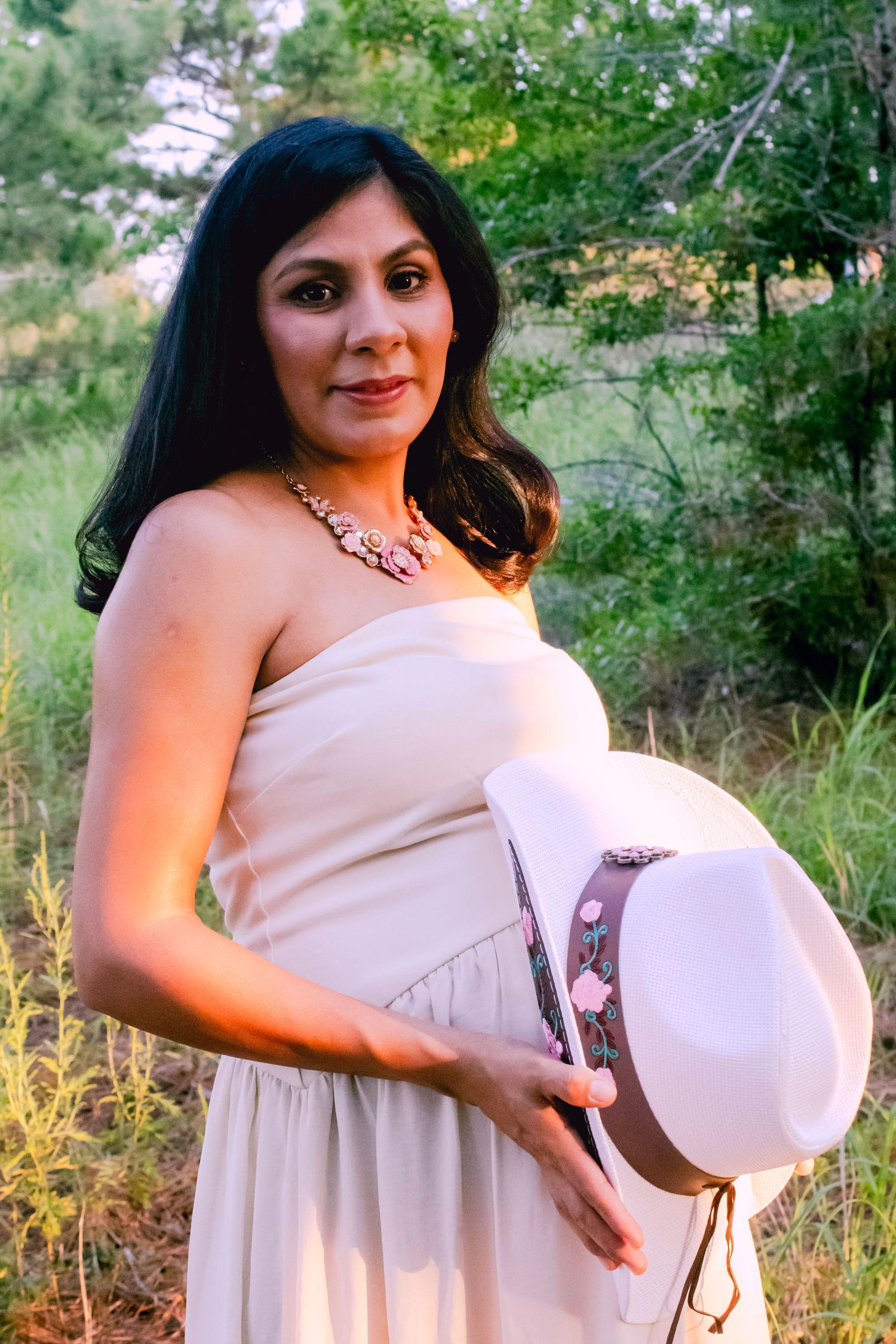 A woman in a flowing cream dress poses outdoors in a natural setting during golden hour.