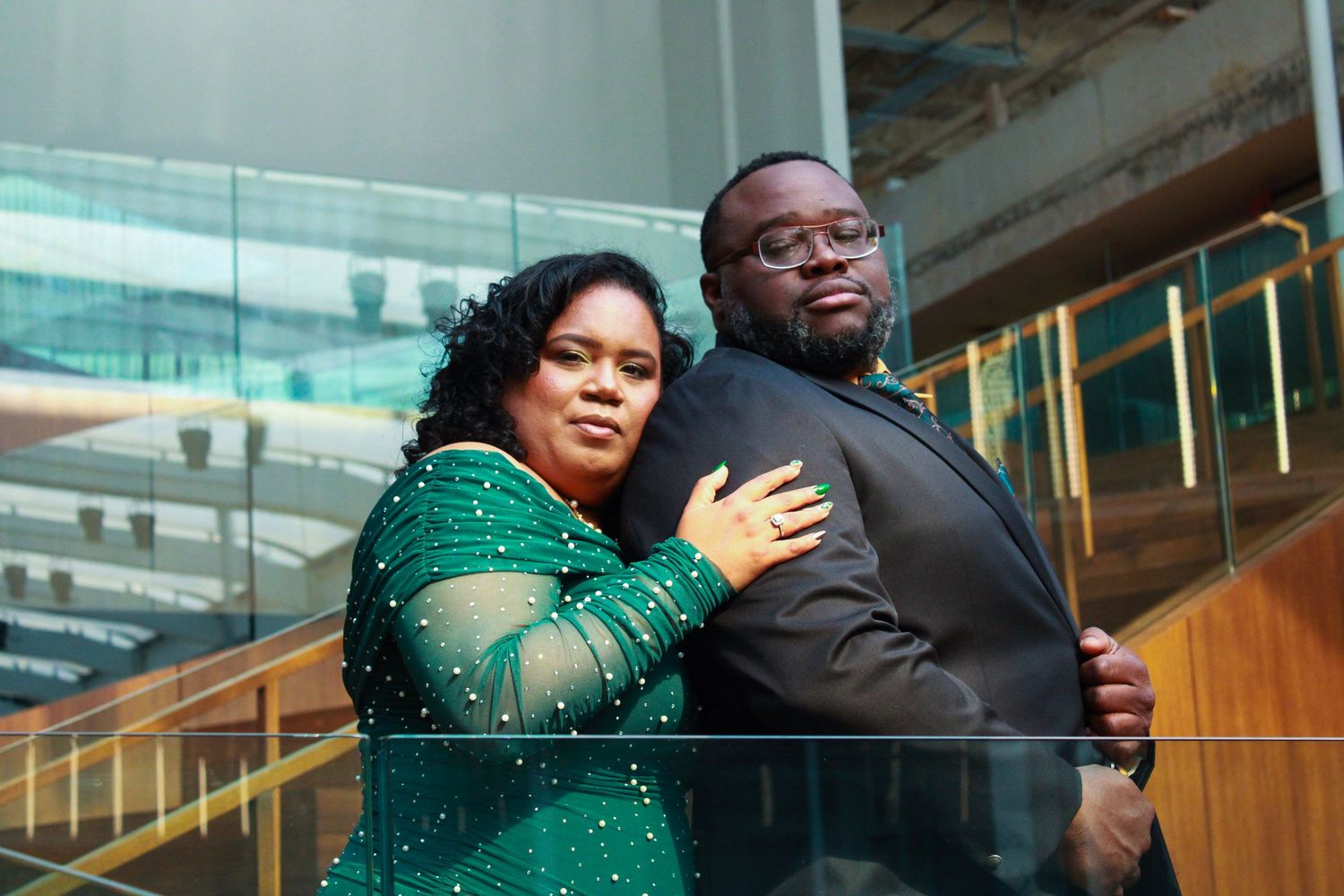 Couple in formal wear embracing in front of modern city architecture.