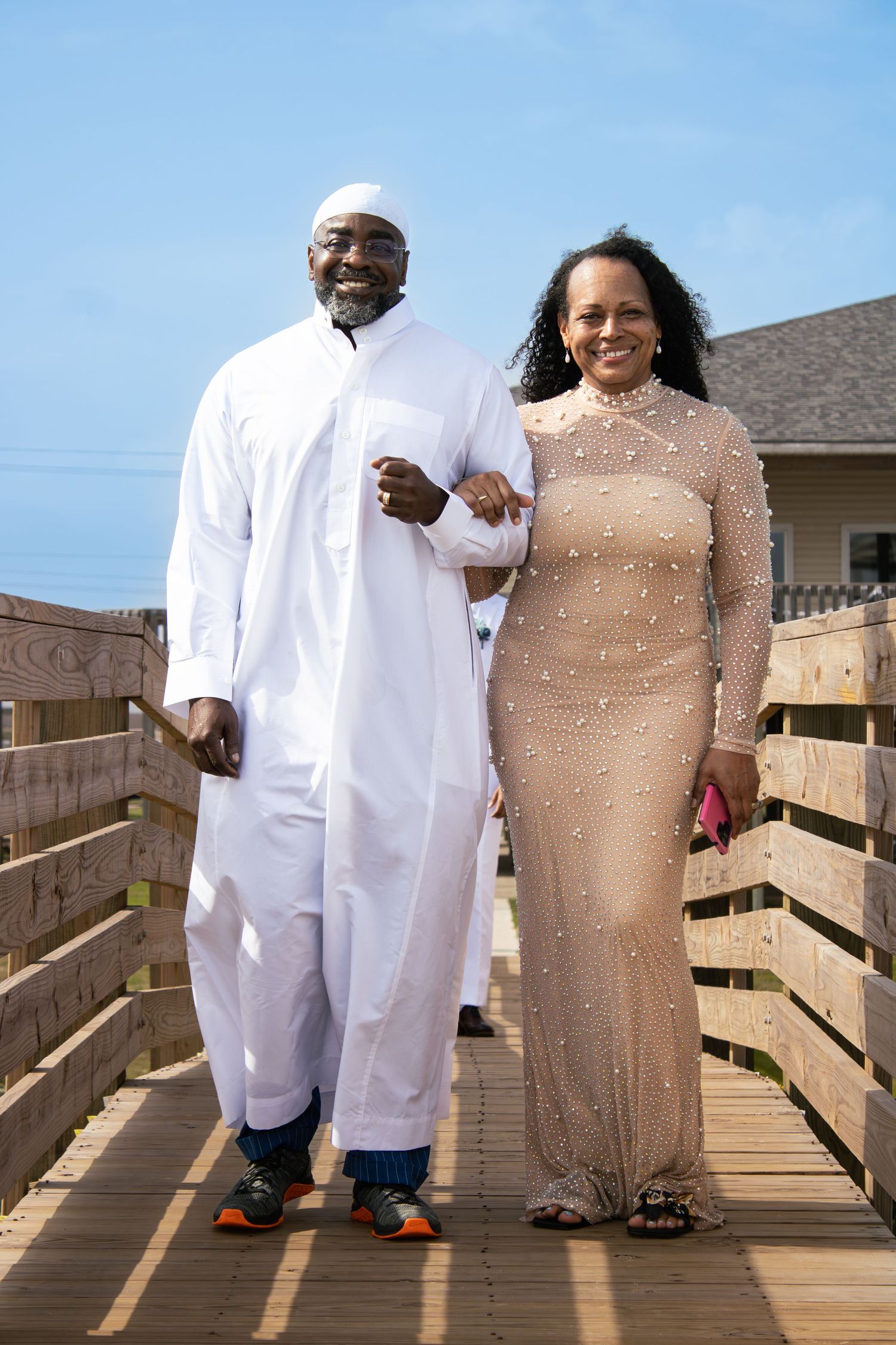 Couple poses on wooden boardwalk wearing white and beige formal attire.