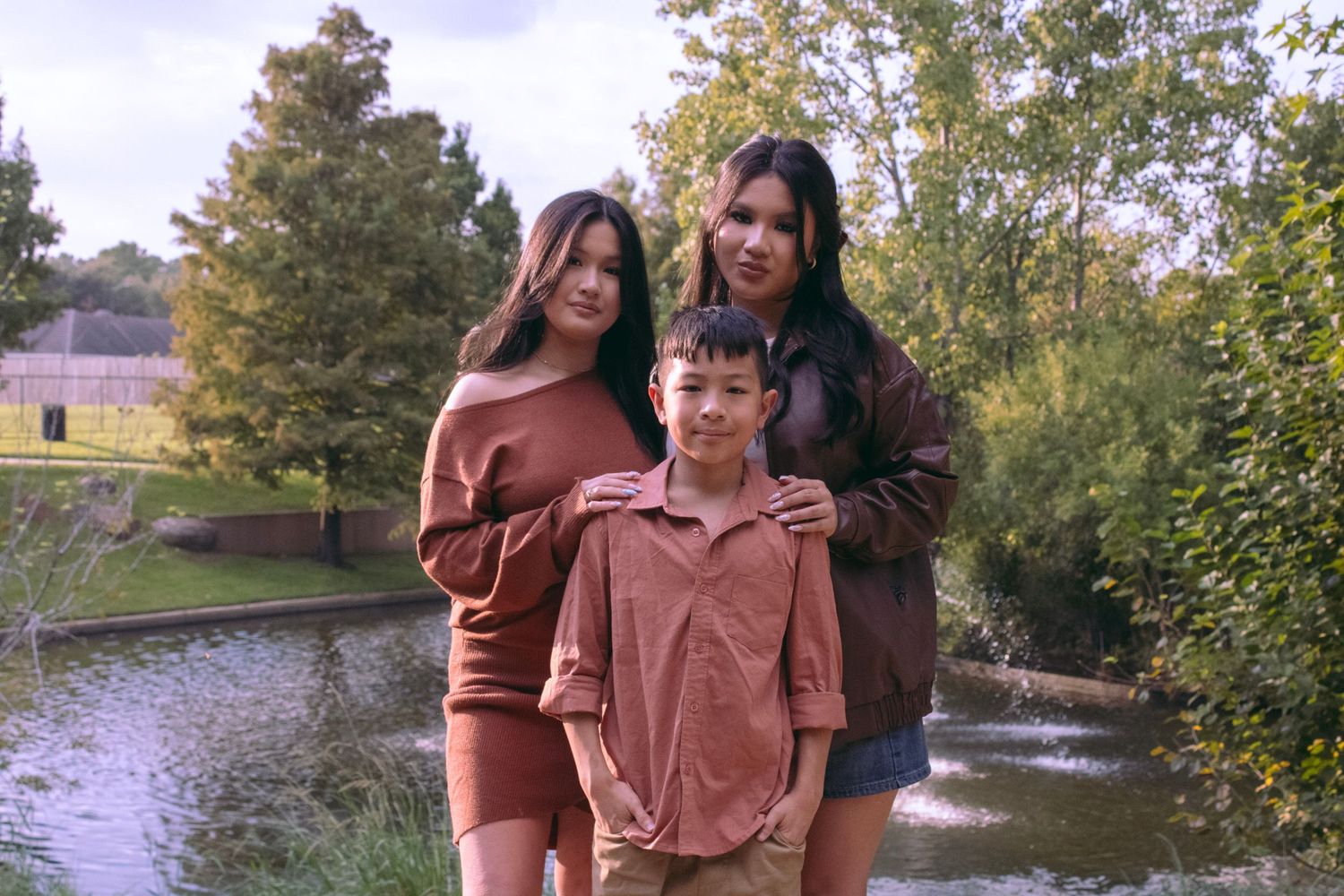 Group photo session by a pond with two doodles wearing coordinated cream-colored sweaters.