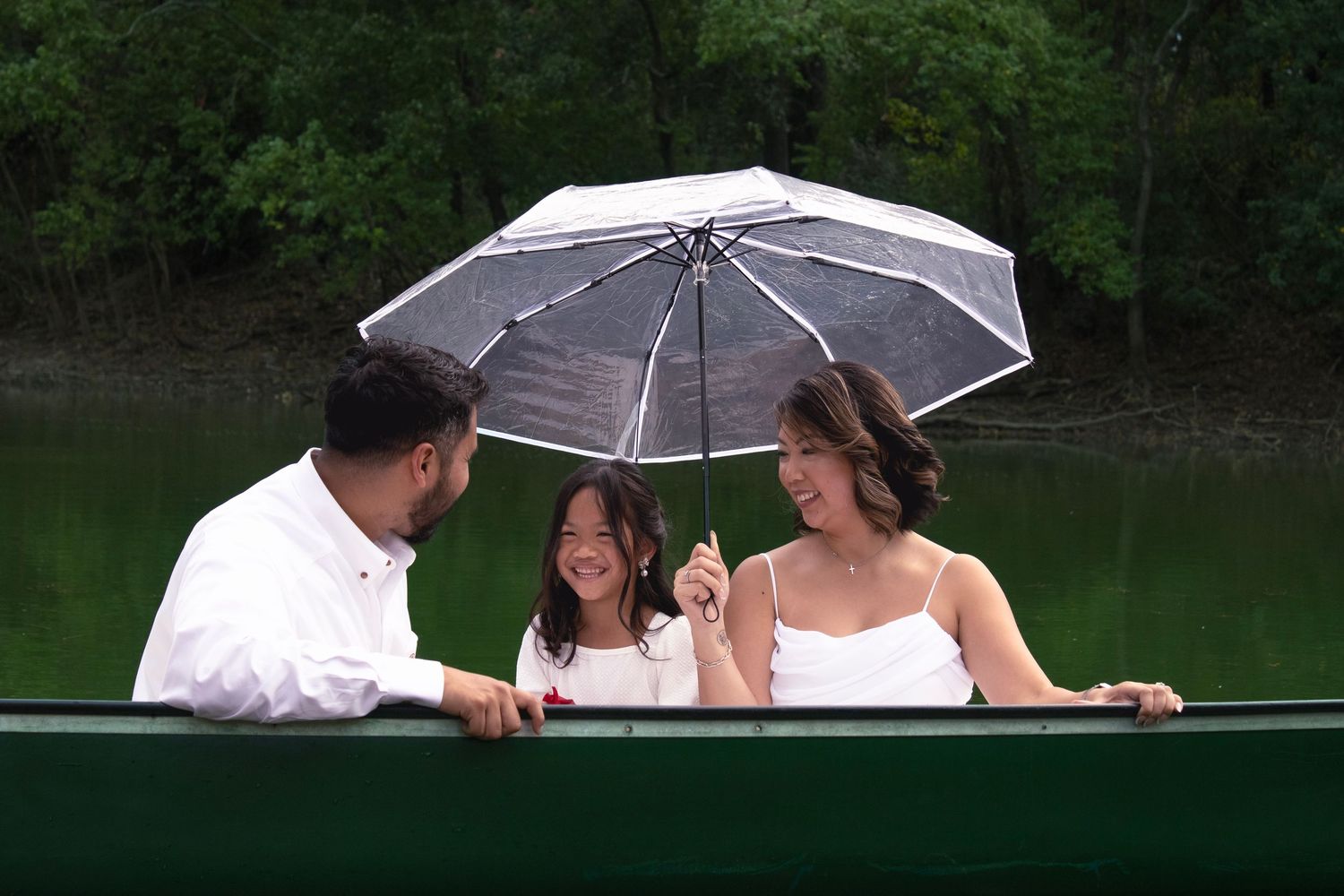 Romantic boat ride featuring couple with clear umbrella on peaceful green lake.