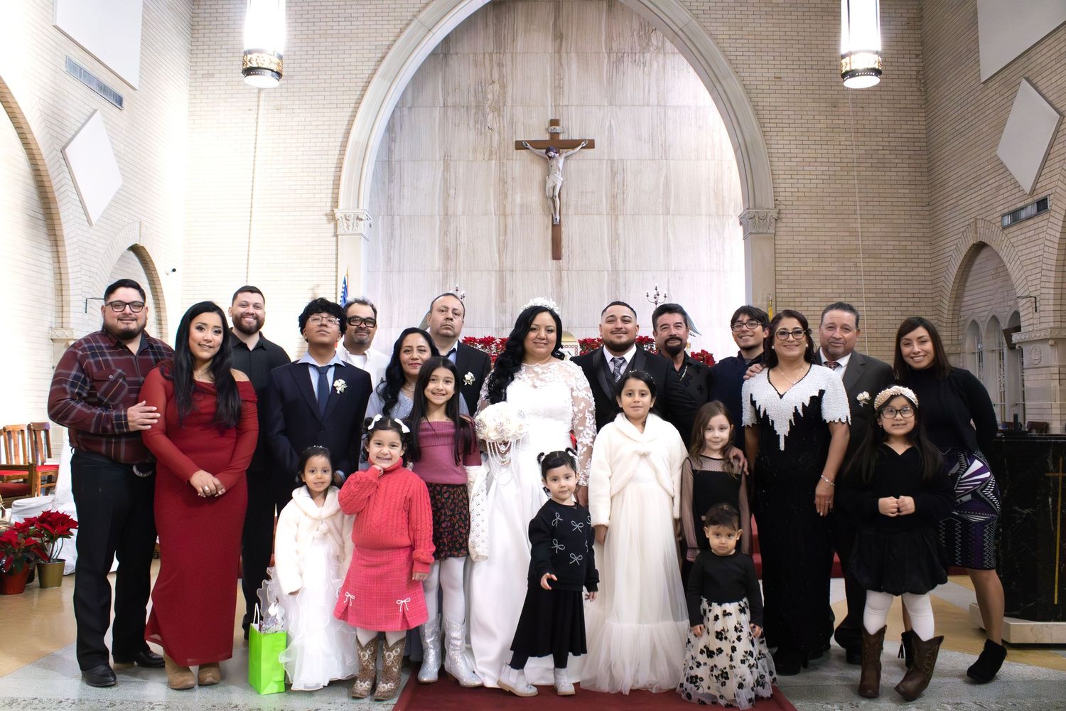 A large group wedding photo inside a church with an arched altar and crucifix.