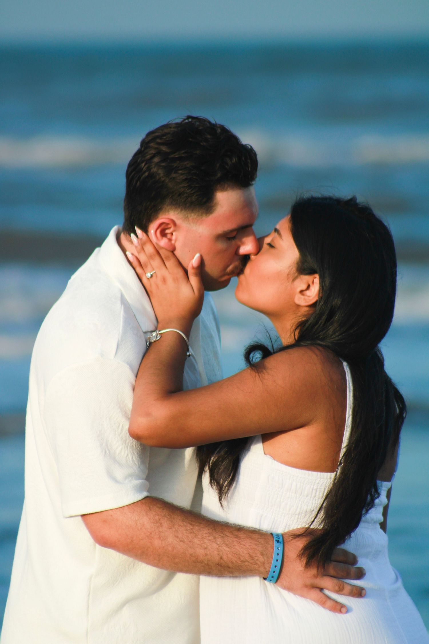 Romantic couple sharing a tender kiss on the beach with ocean waves in the background.
