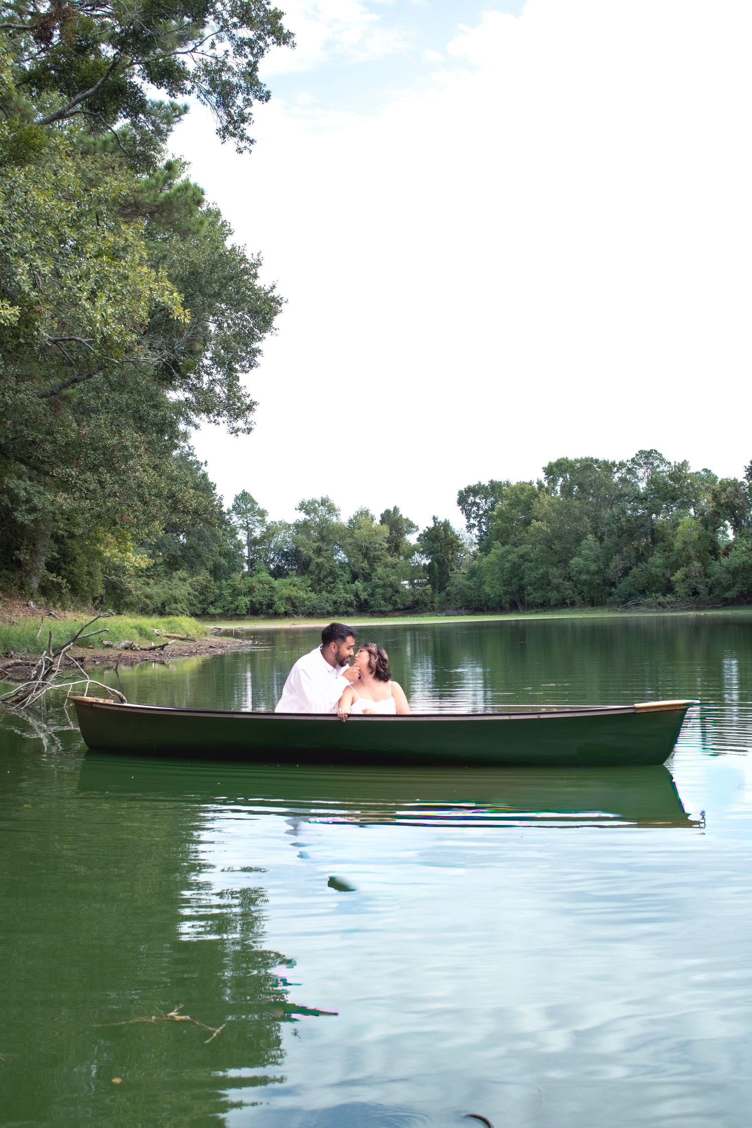 A romantic couple shares an intimate moment while sitting in a canoe on a serene lake.