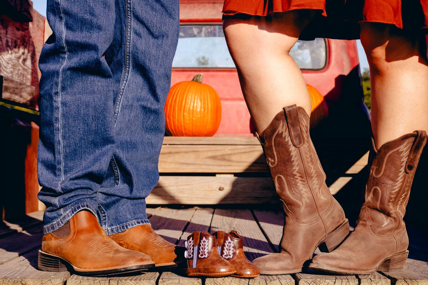 Cowboy boots and tiny baby shoes arranged on wooden steps with a pumpkin.