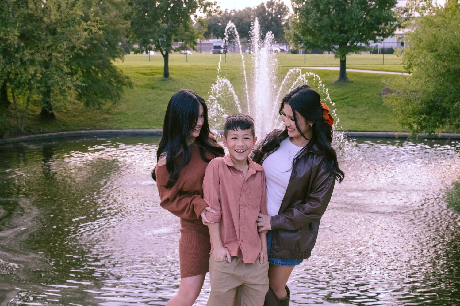 Outdoor photo session near a pond with two dogs and their family in coordinated outfits.