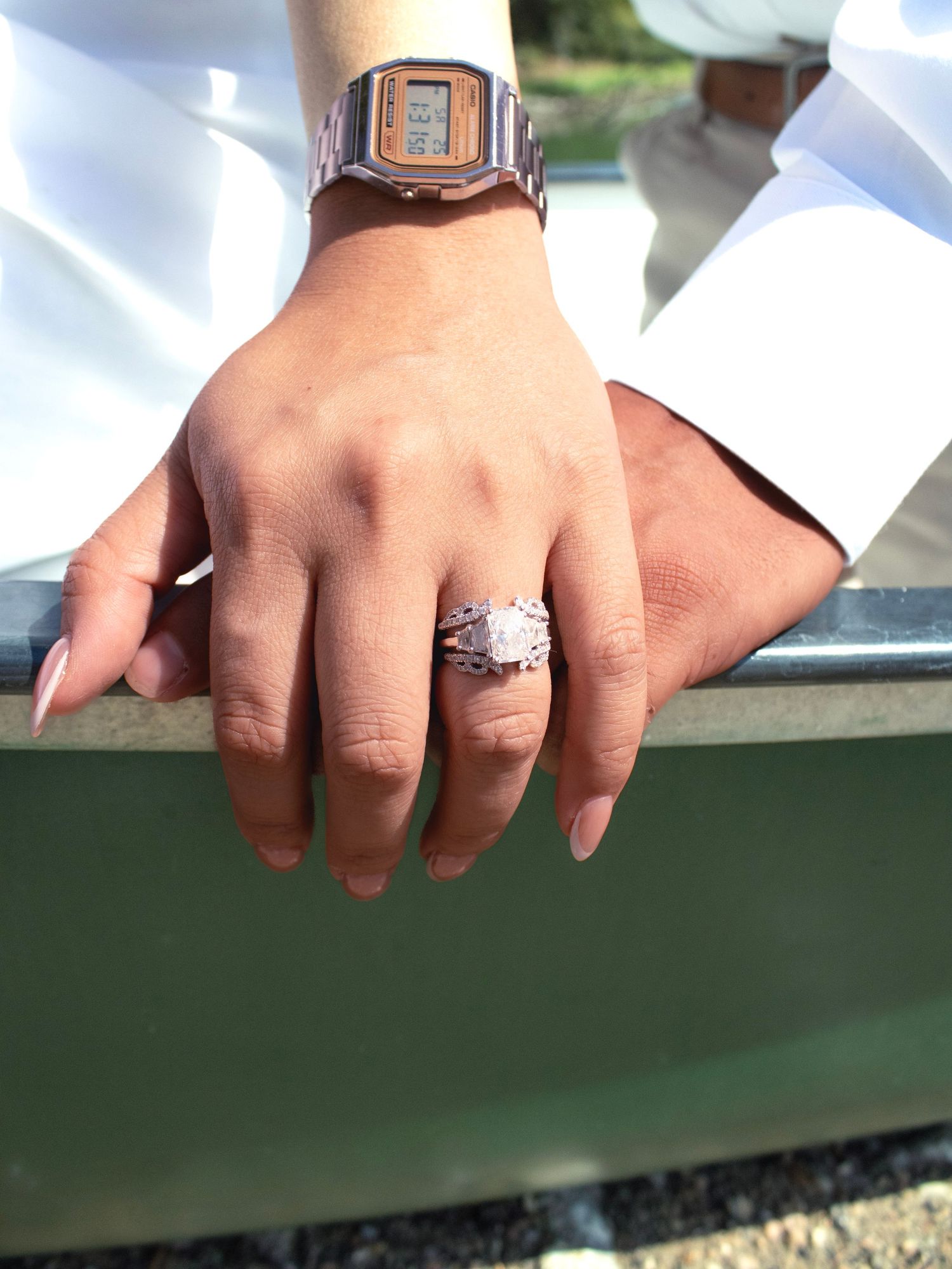 Close-up of hands showing off an engagement ring and watch against a boat railing.