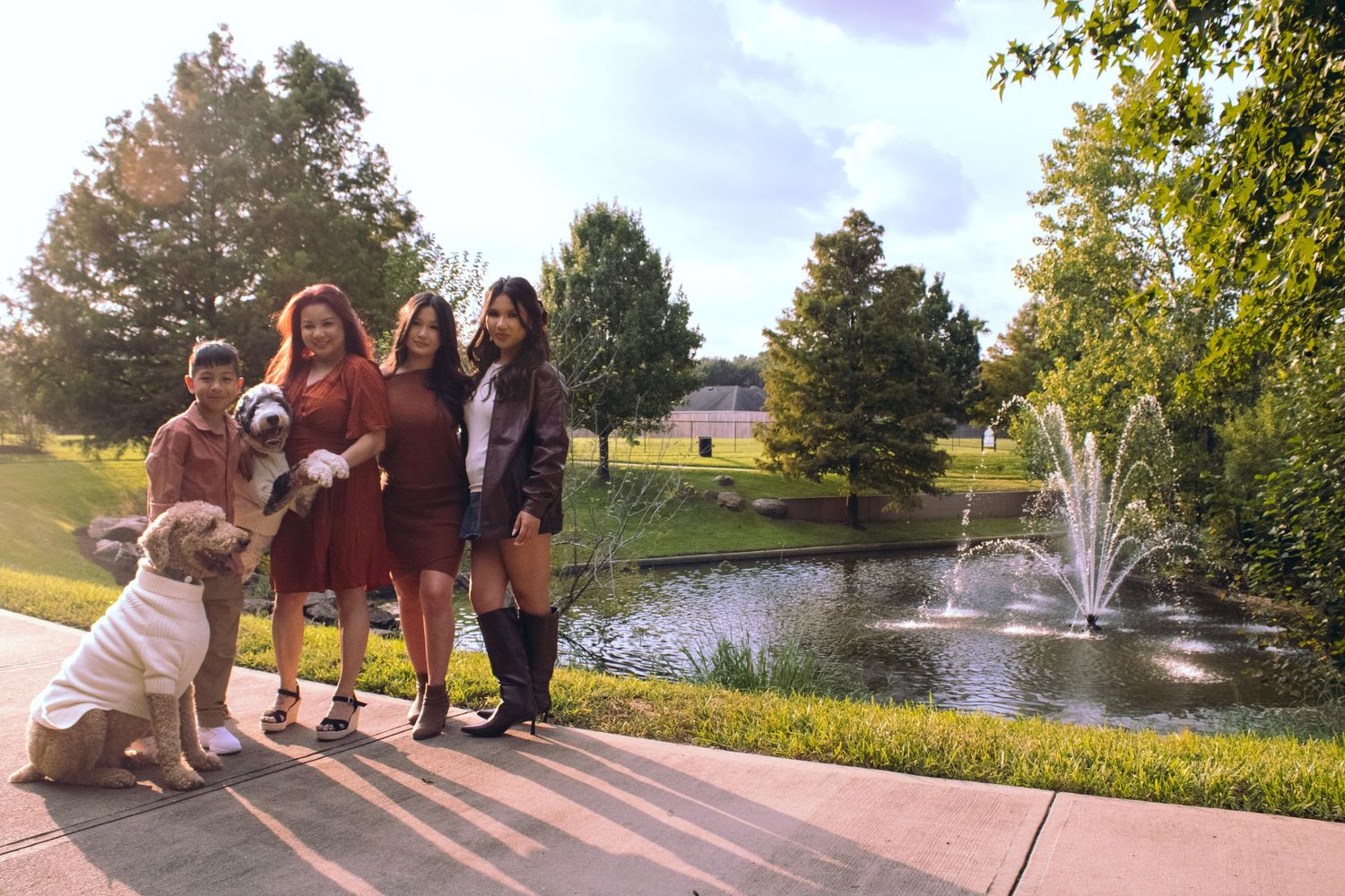 Family portrait session with two doodles by a pond featuring a fountain on a sunny day.