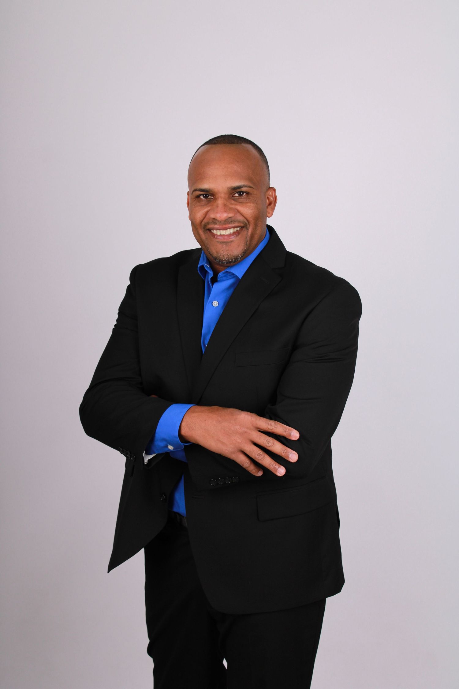 Professional headshots of a person in a black suit and blue shirt against a gray background.