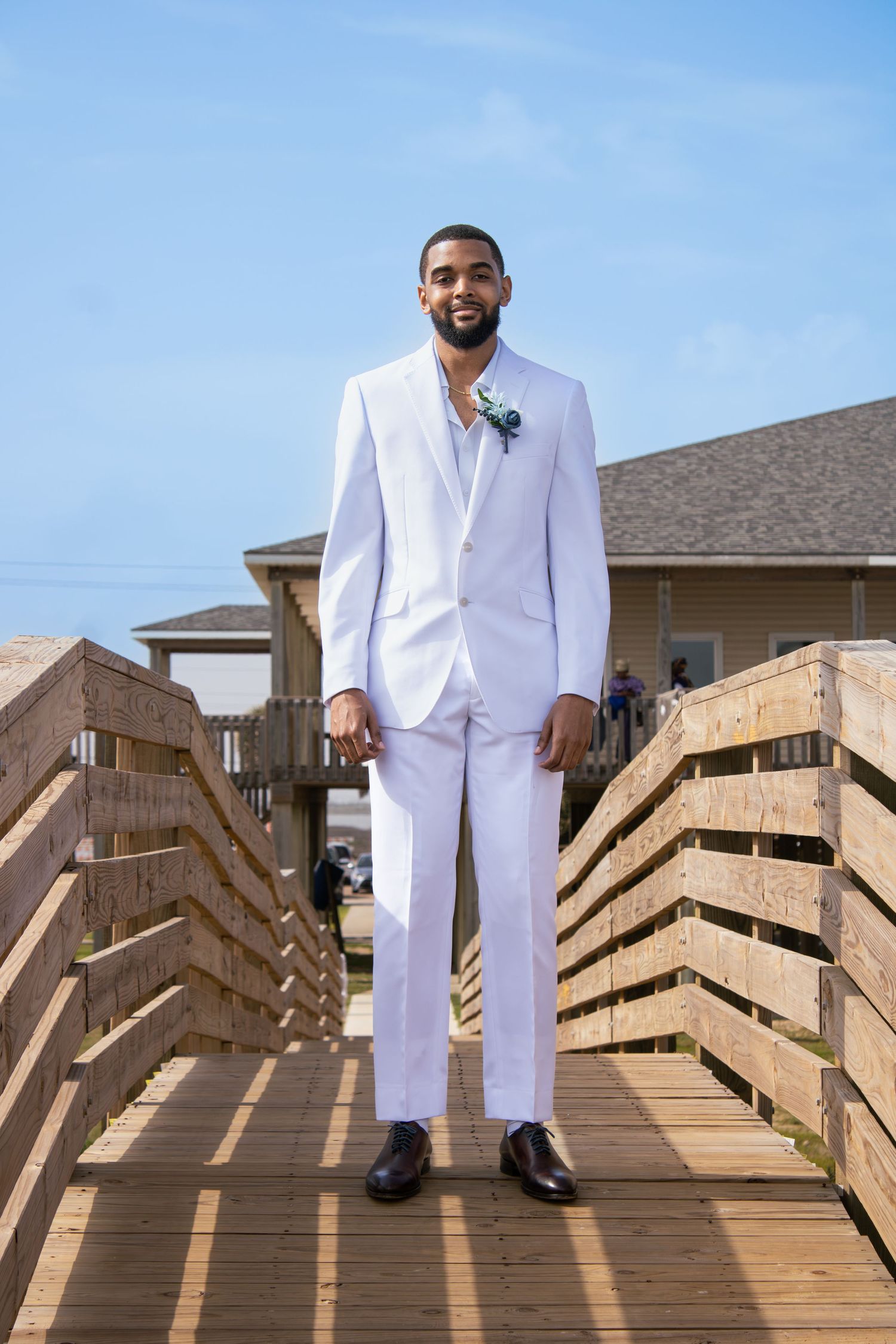 Wedding photos on wooden boardwalk with formal white attire against blue sky backdrop.