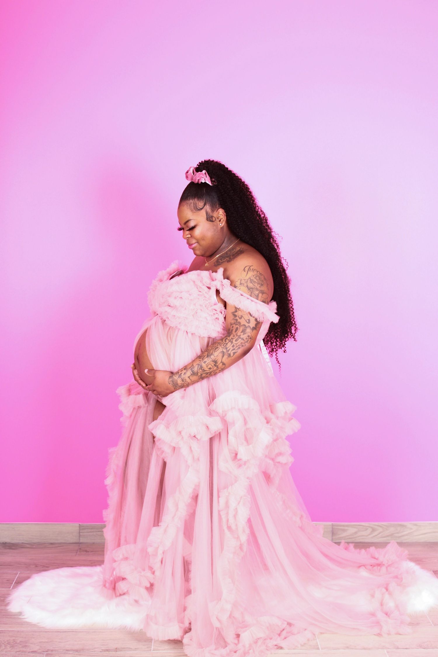 Dreamy maternity photos with billowing pink gown against pastel background.