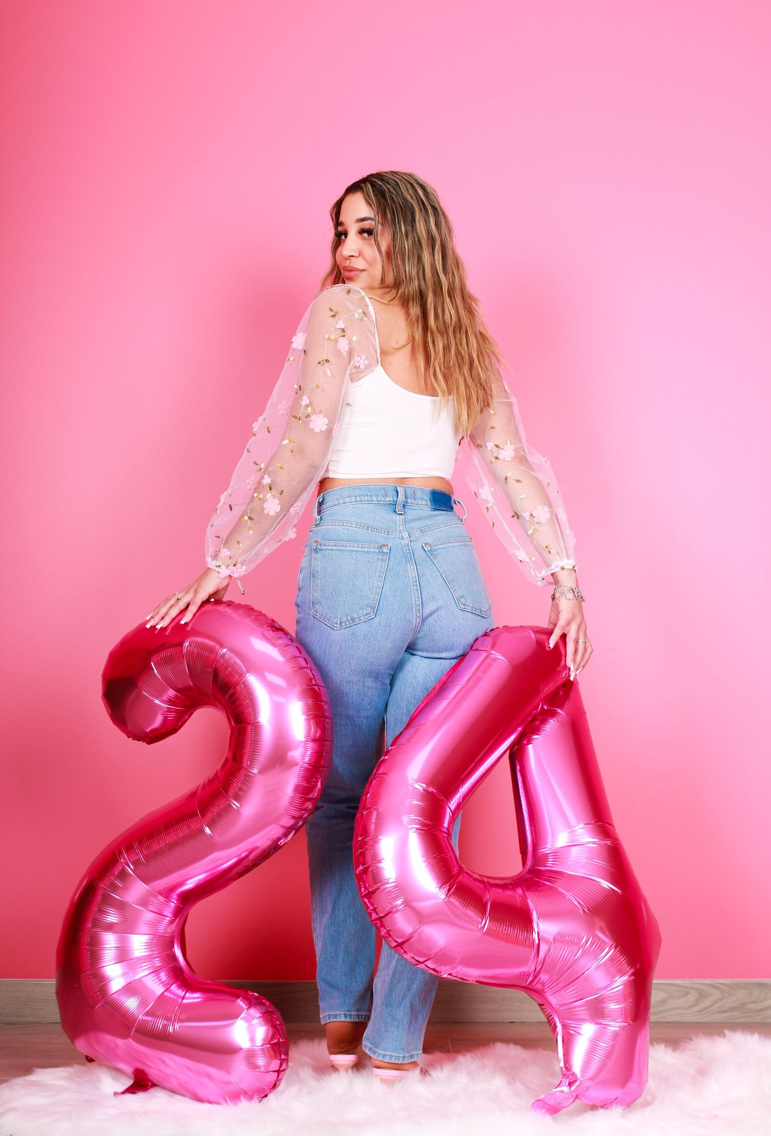 Decorative pink number balloons arranged with white furry rug against pink backdrop.