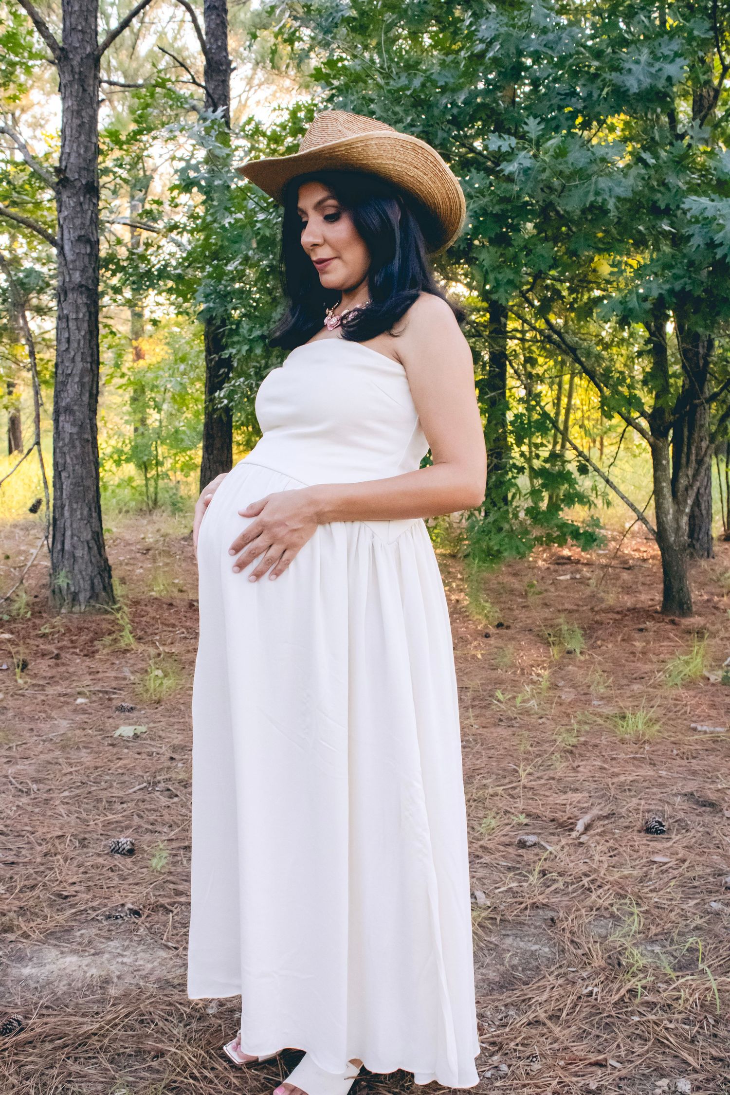 A flowing white maternity dress contrasts beautifully against a forest backdrop.