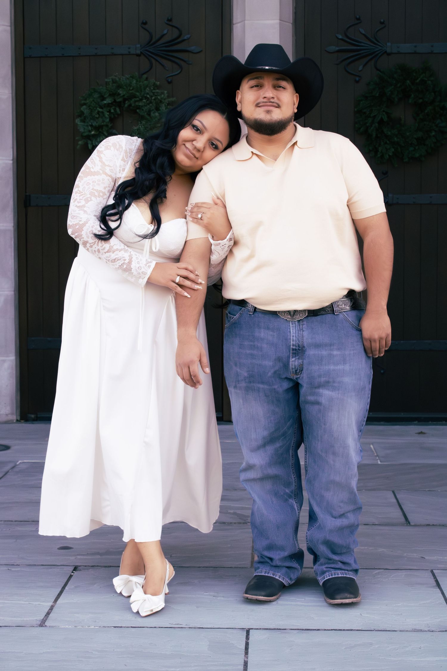 A couple in wedding attire poses together outside a building.