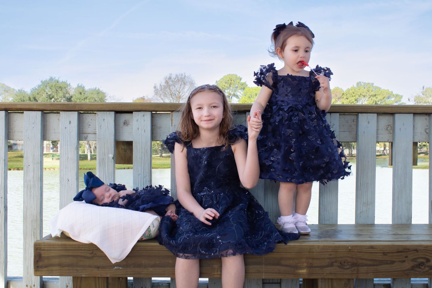 Sisters in matching navy blue dresses pose on wooden deck railing.