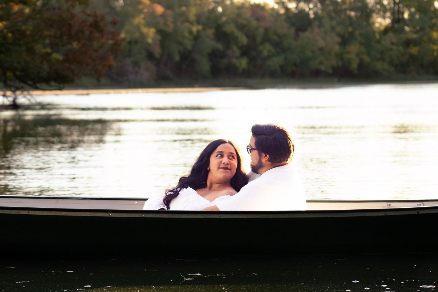 A silhouetted couple in a boat against a sunset-lit lake.