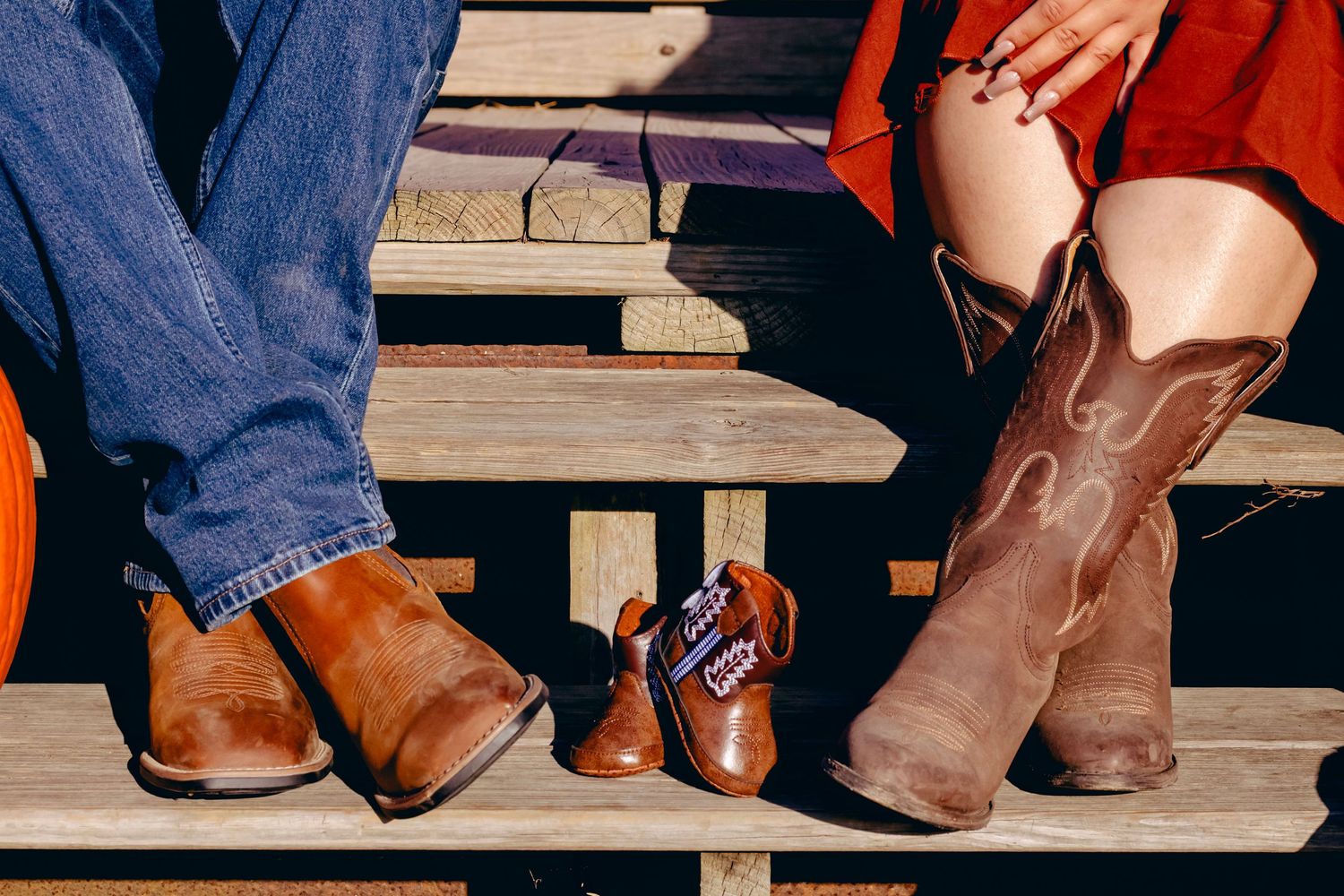 Brown cowboy boots and shoes arranged on wooden steps with jeans and orange fabric.
