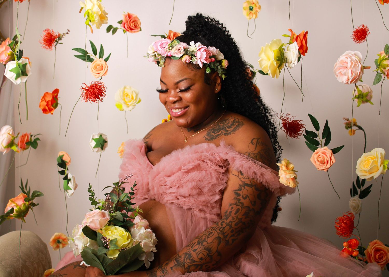 Whimsical maternity photos with hanging colorful flowers and pink dress.