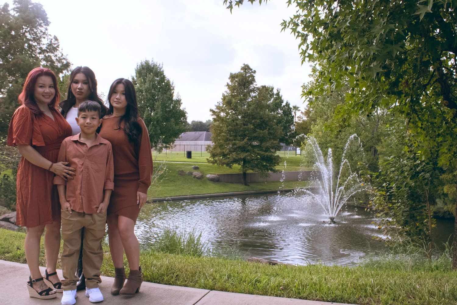 Outdoor family photoshoot with two goldendoodles near a scenic pond with fountain.