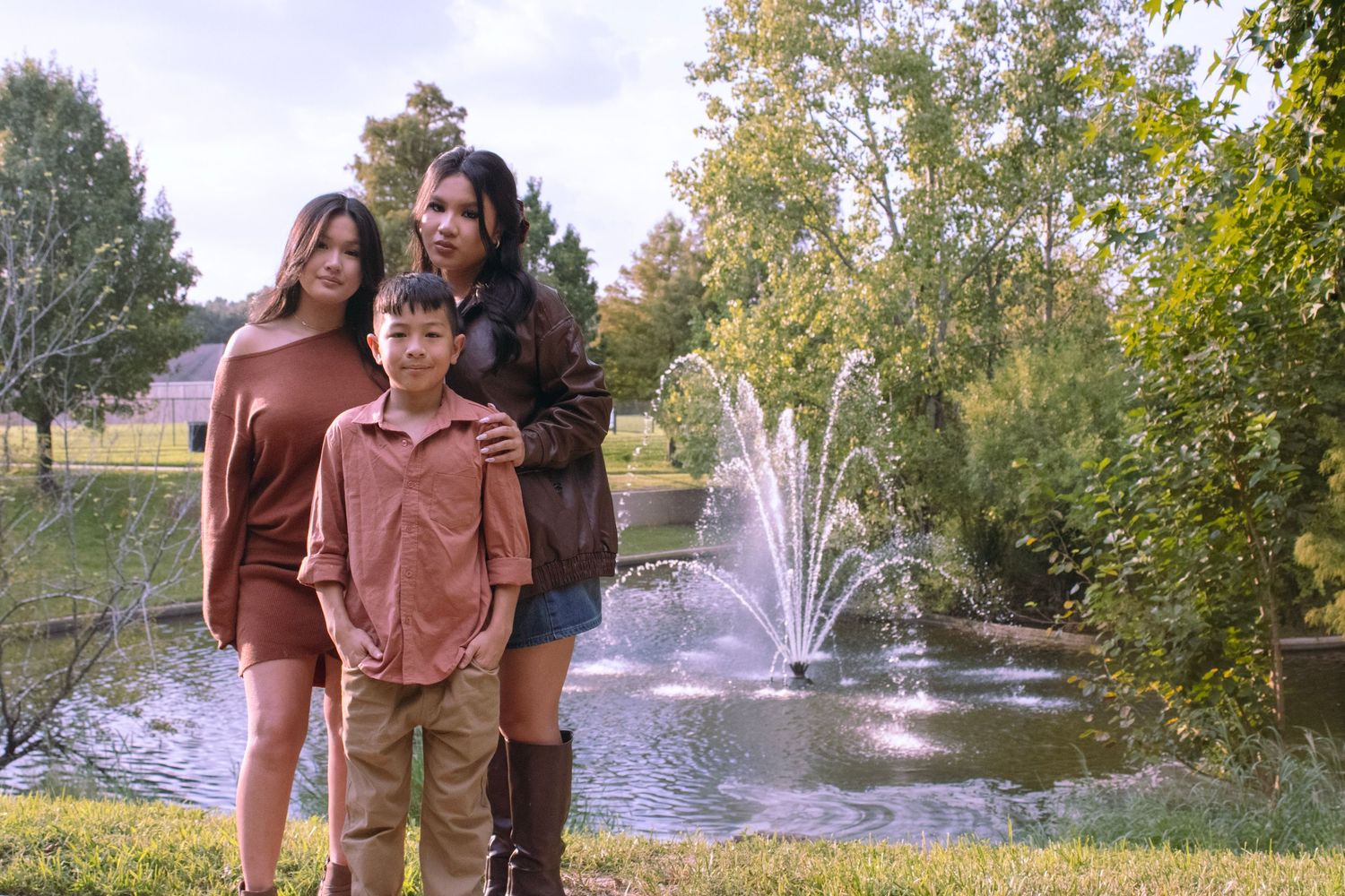 Family and their doodle dogs gather for photos near a pond with a fountain on a sunny autumn day.