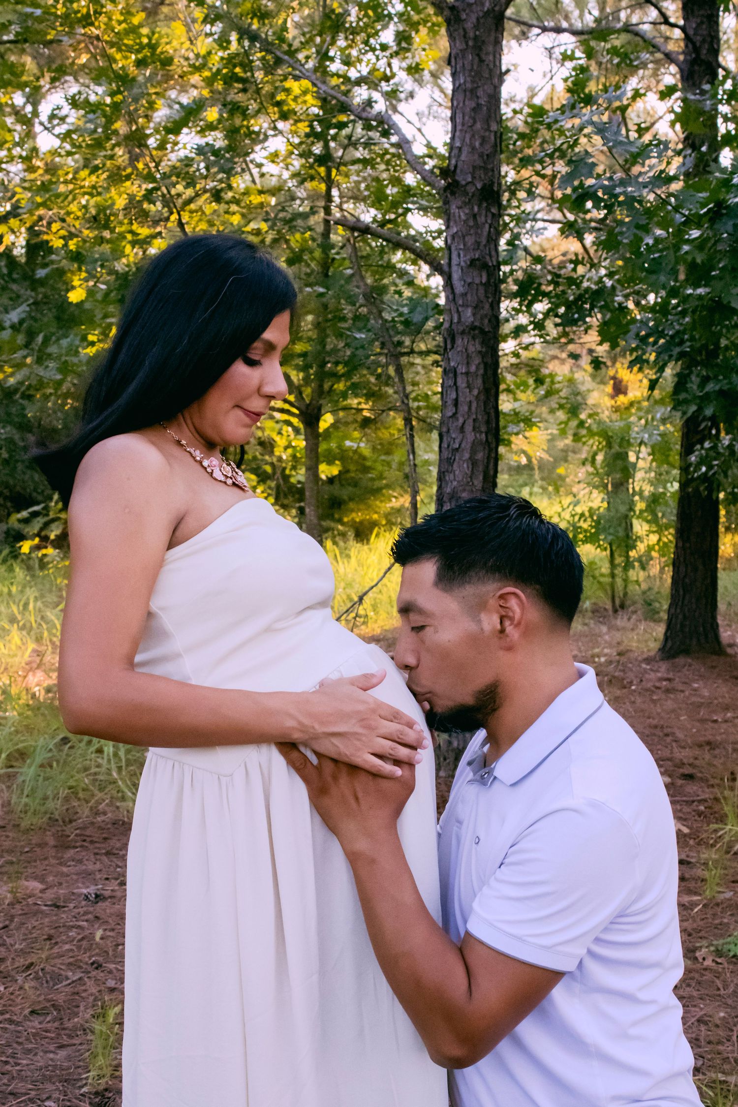 A tender maternity moment captured in a forest setting during golden hour.