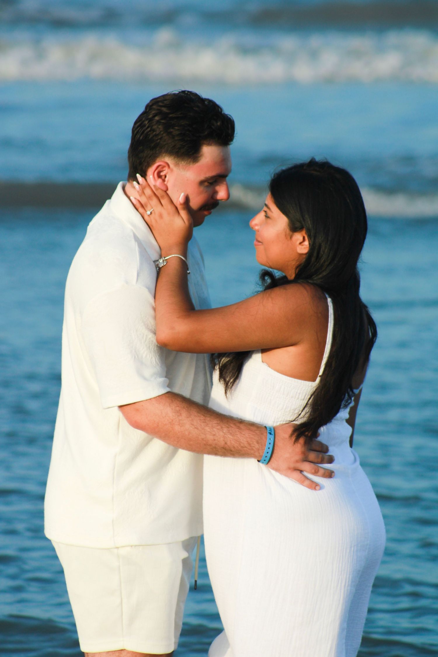 Romantic couple embracing on beach at sunset with ocean waves in background.