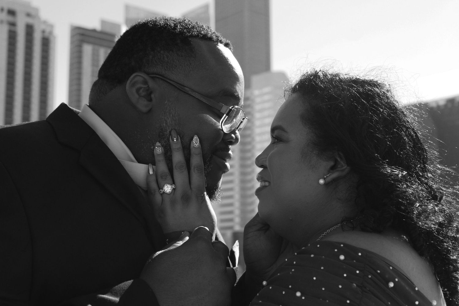 Monochrome portrait of couple with city buildings in background.