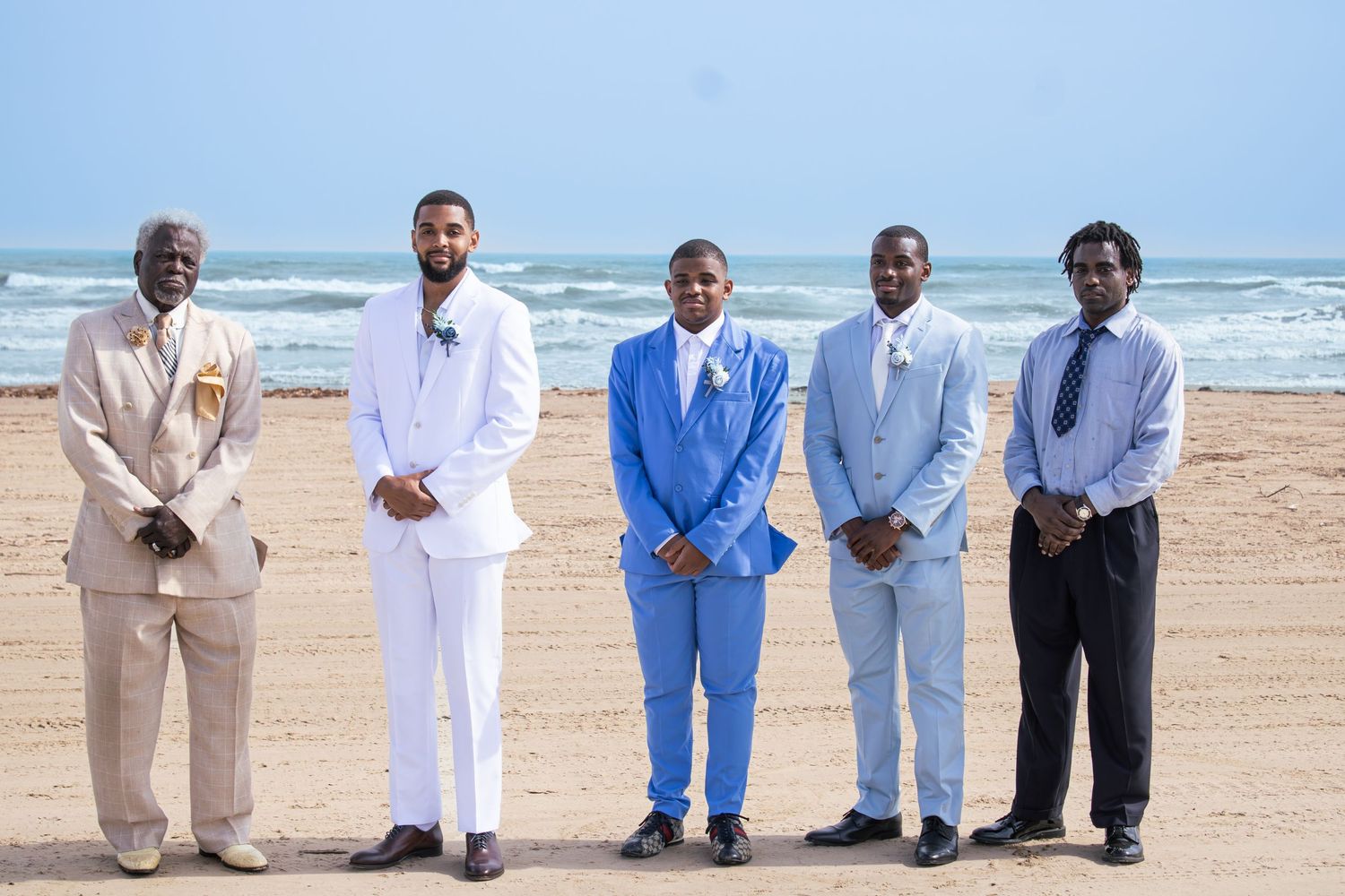Wedding party lined up on beach wearing coordinated white and light blue formal attire.