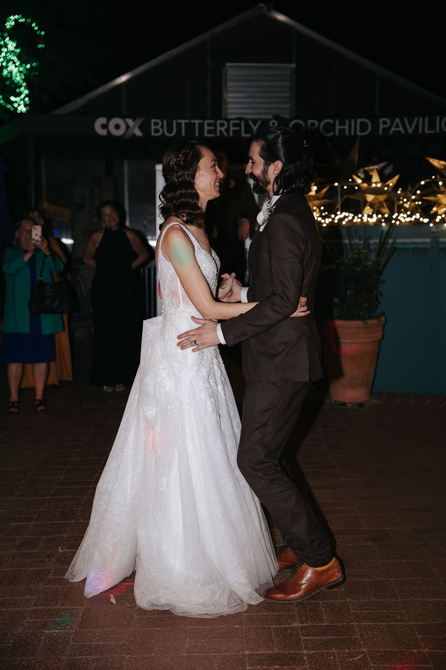 A couple shares their first dance at a nighttime wedding reception outside the Cox Butterfly Orchid Pavilion.