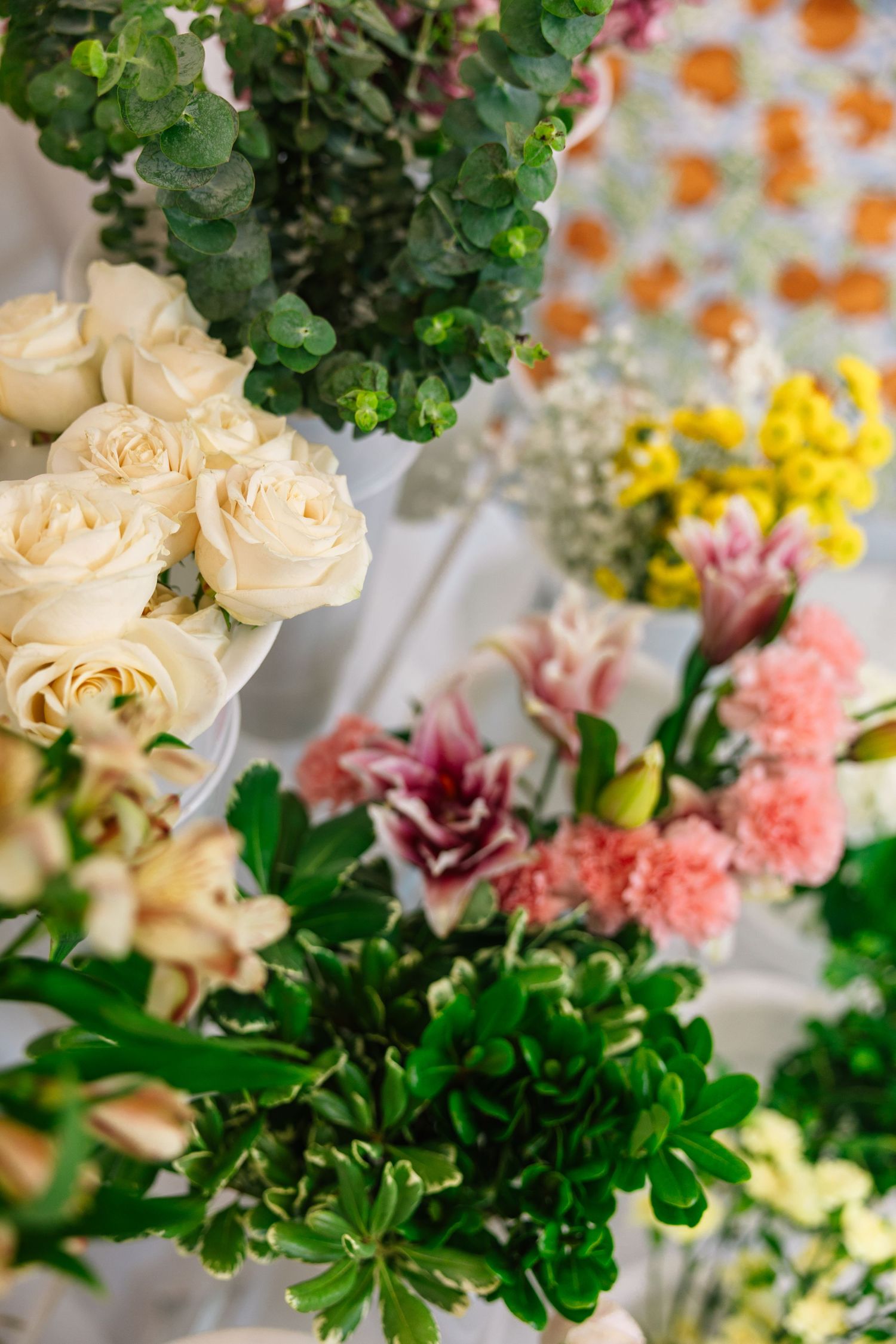 Close-up of fresh floral arrangement with cream roses, pink carnations, yellow flowers and green foliage in soft focus.