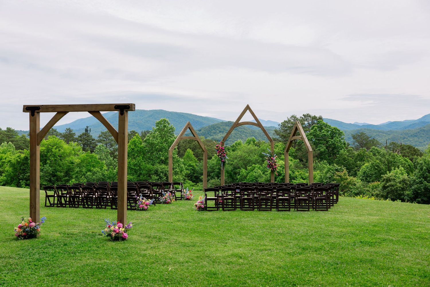 A scenic panoramic view of a rustic wedding venue with wooden pergolas set against rolling green mountains.