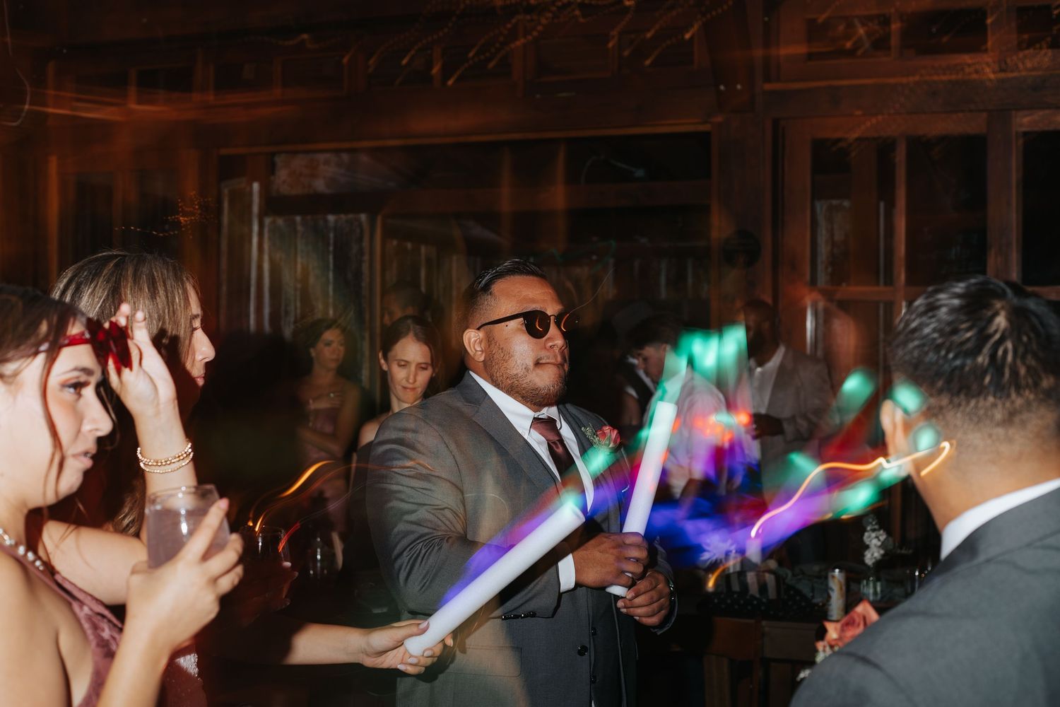 People dancing and having fun at a dimly lit wedding reception with colorful lights illuminating the dance floor.
