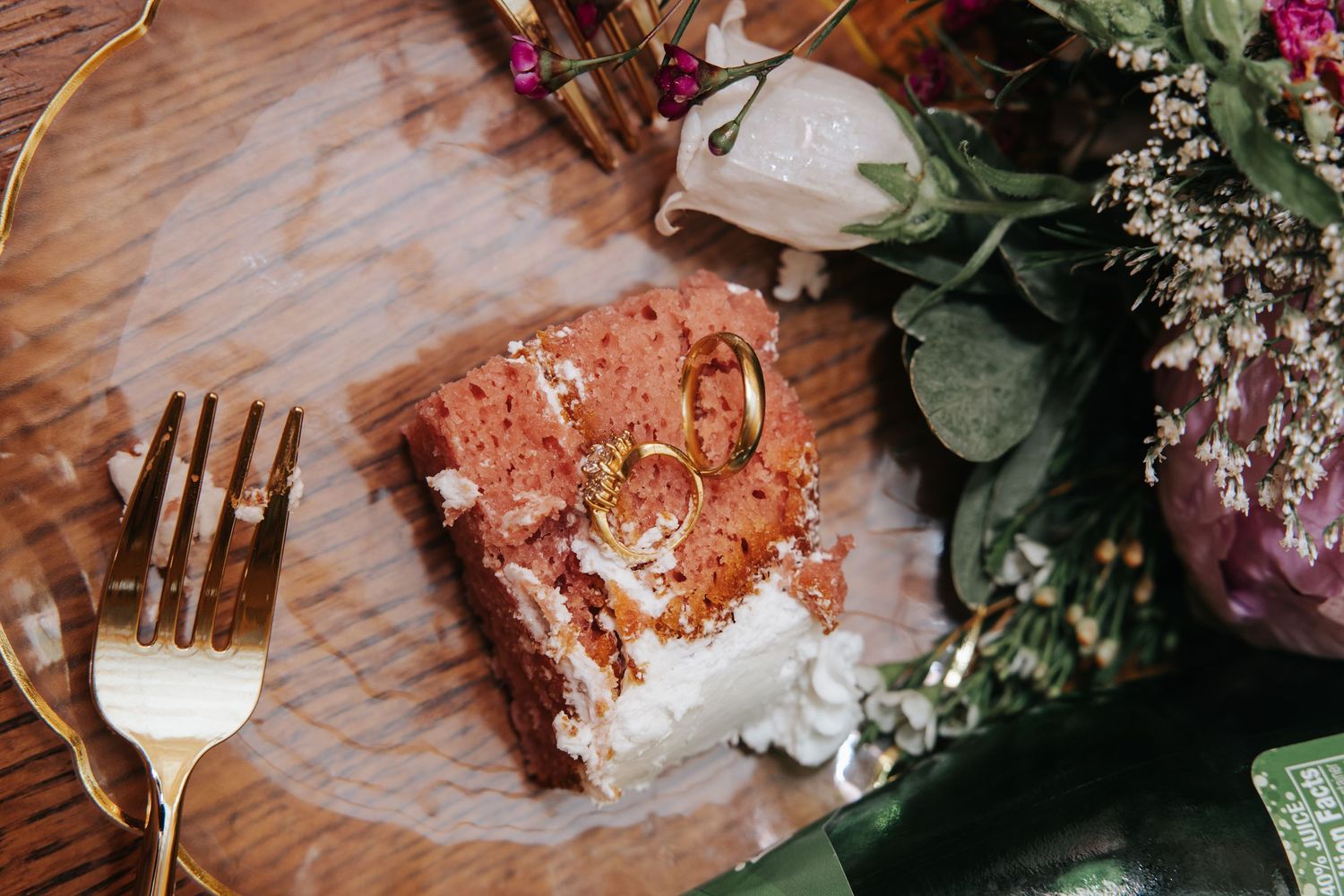 A rustic wooden table setting adorned with pink flowers, eucalyptus leaves, and elegant gold flatware for a wedding reception.