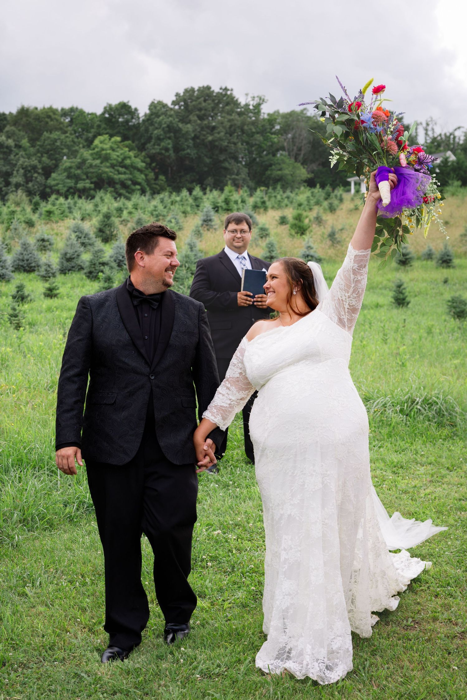 A couple in wedding attire dances joyfully together in a green field during their outdoor celebration.