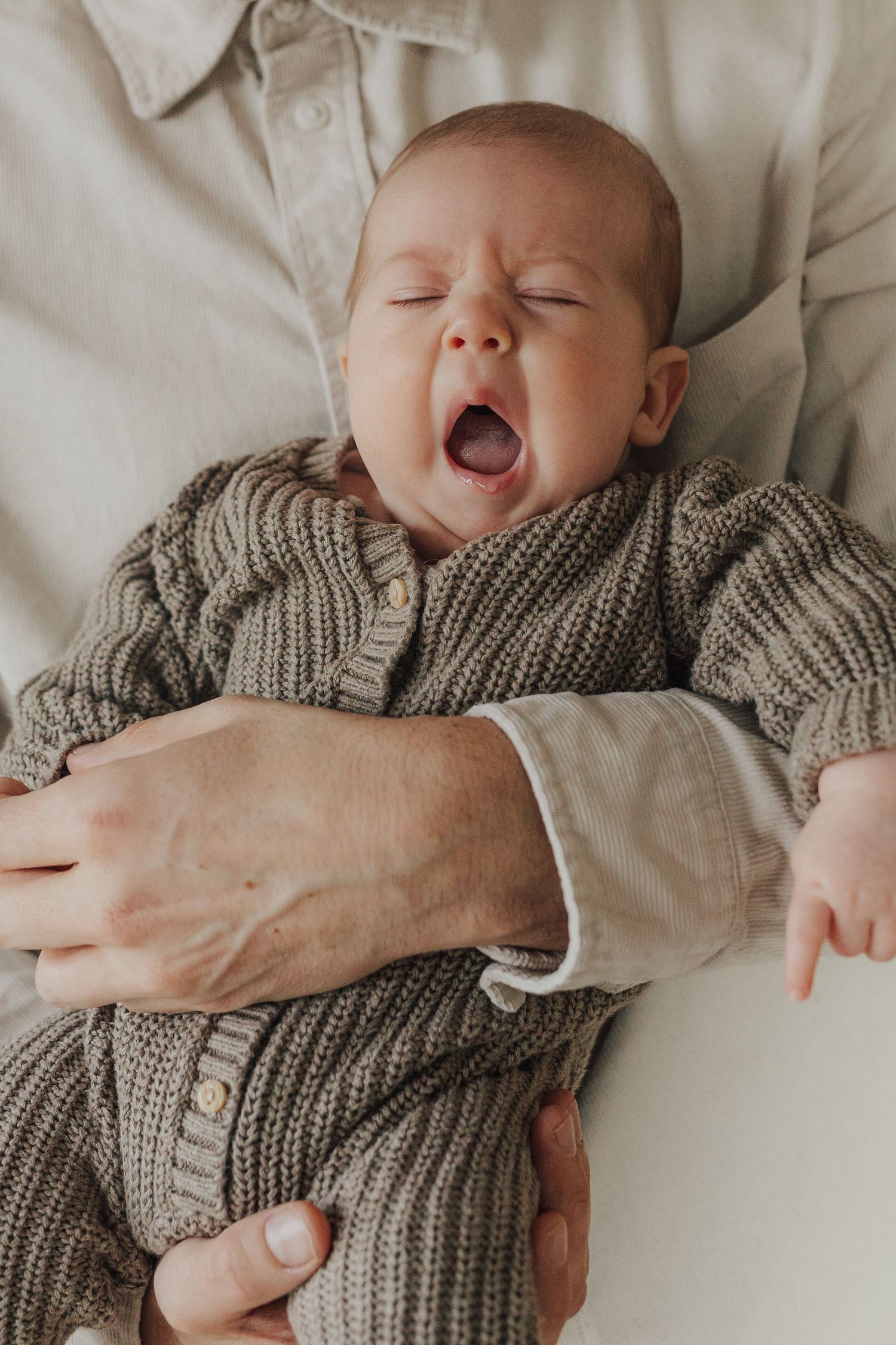 Sleeping newborn wrapped in cozy gray knit blanket in peaceful posed portrait series.