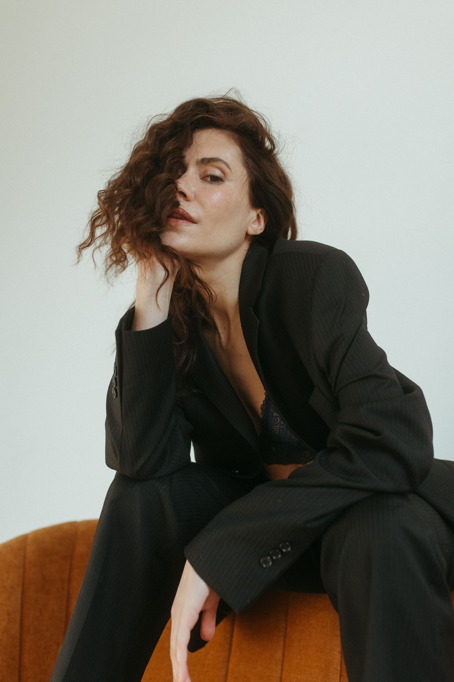 Artistic portrait series showing model in oversized black blazer on brown couch.