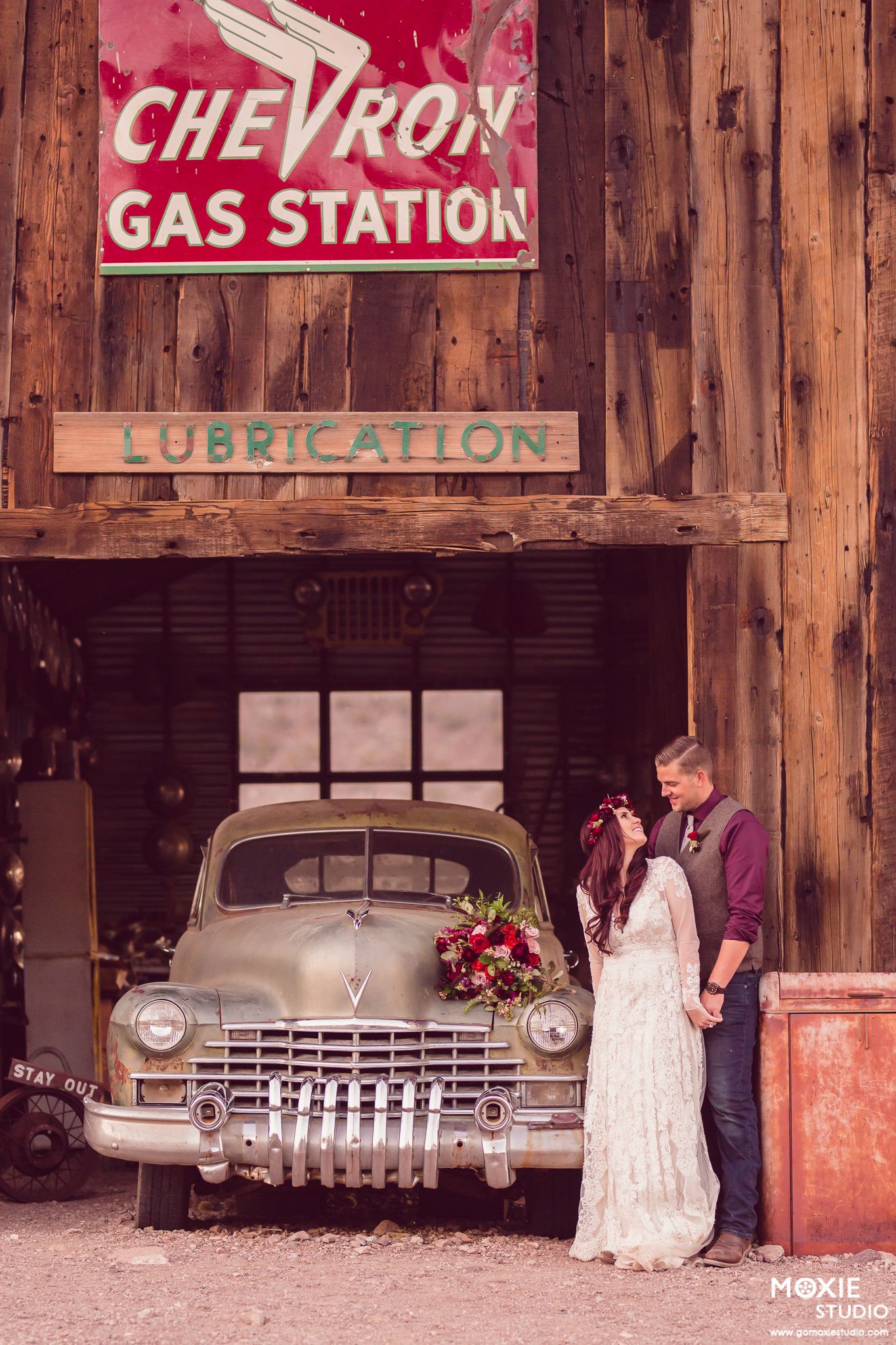 Vintage Chevron gas station with classic cars parked inside wooden garage bays and retro signage.