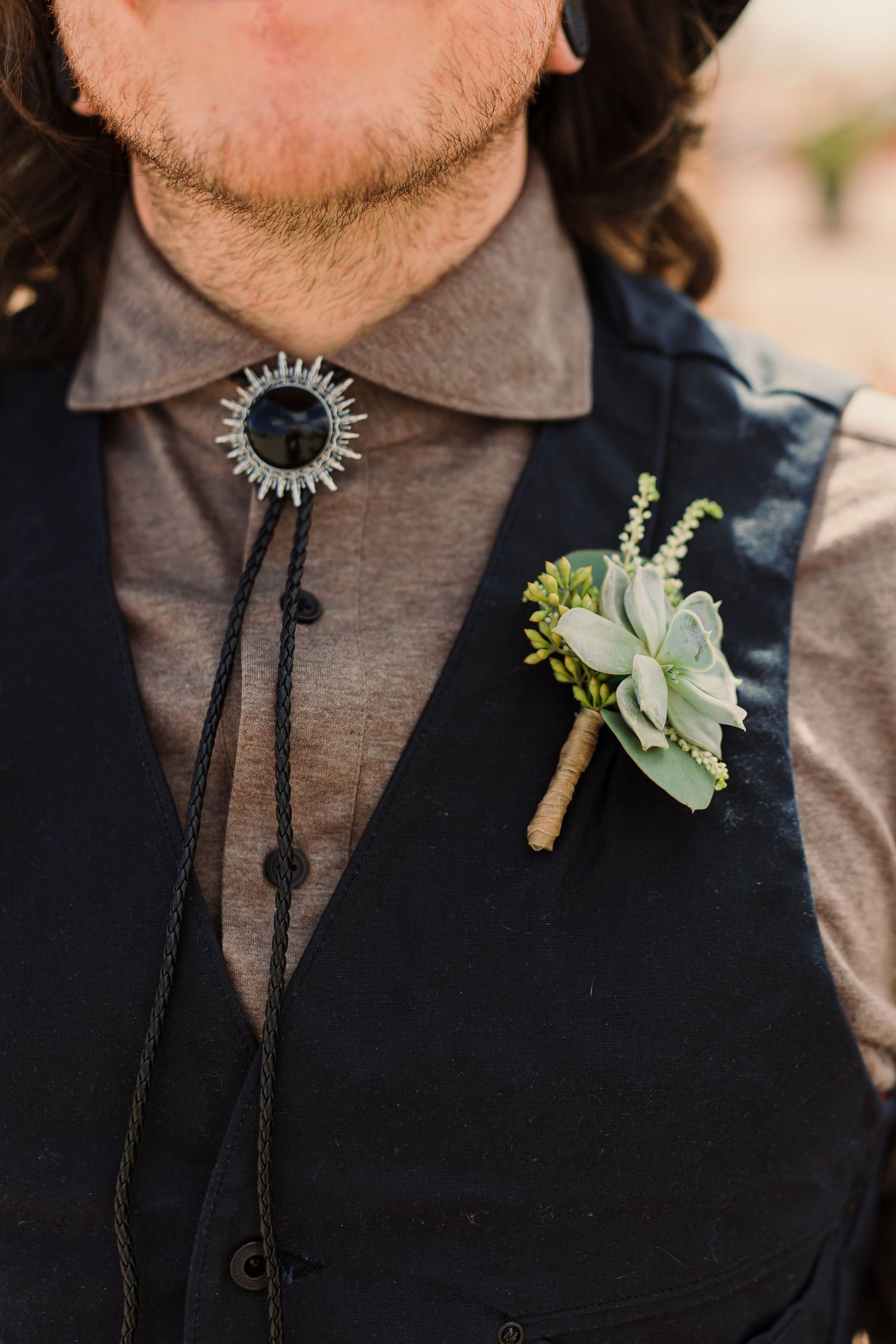 Close-up detail of a black vest with a succulent boutonniere and bolo tie.