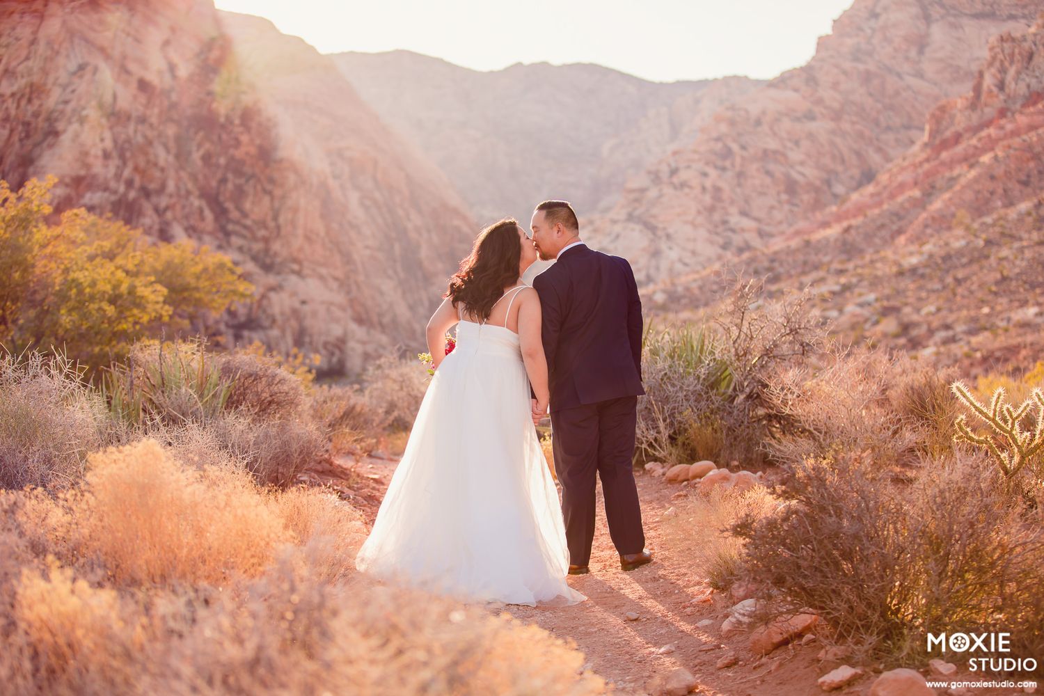 A couple in wedding attire walking together at sunset in a scenic desert canyon landscape.