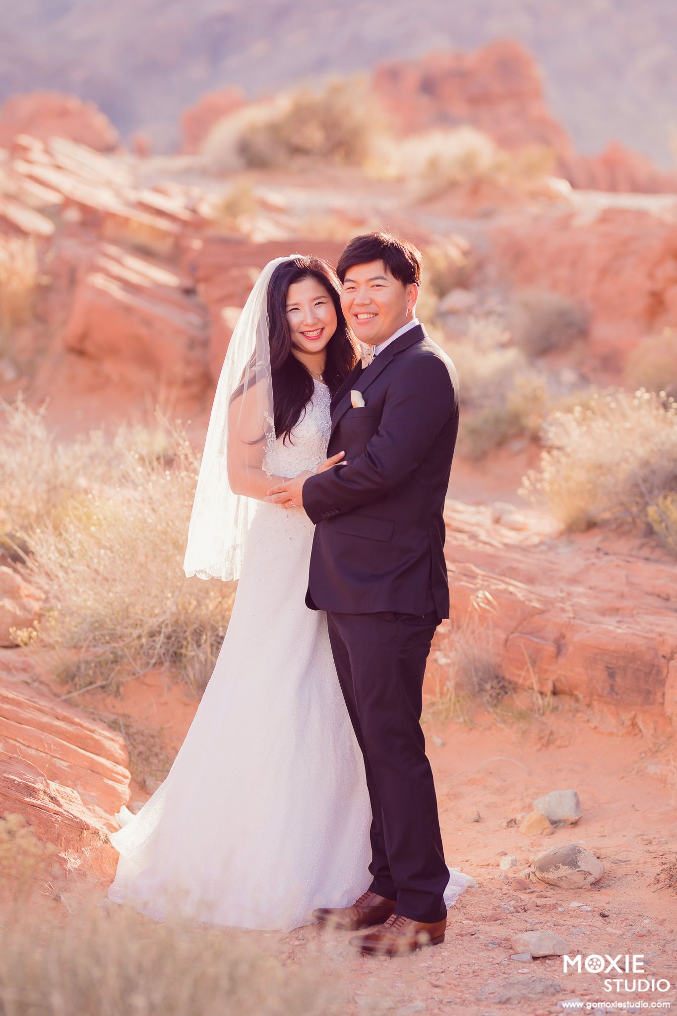 A romantic wedding photo session in a desert landscape with red rocks and golden light at sunset.
