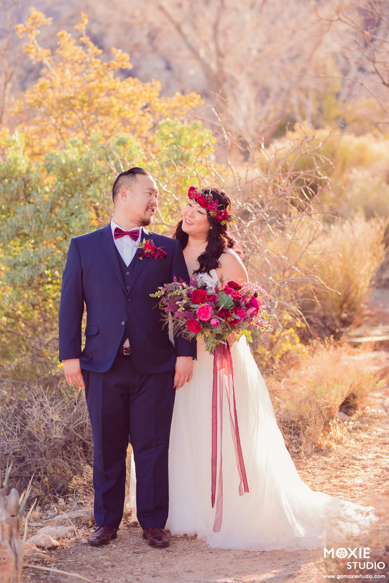 Romantic desert wedding scene with couple in white dress and dark suit against golden sunset backdrop.