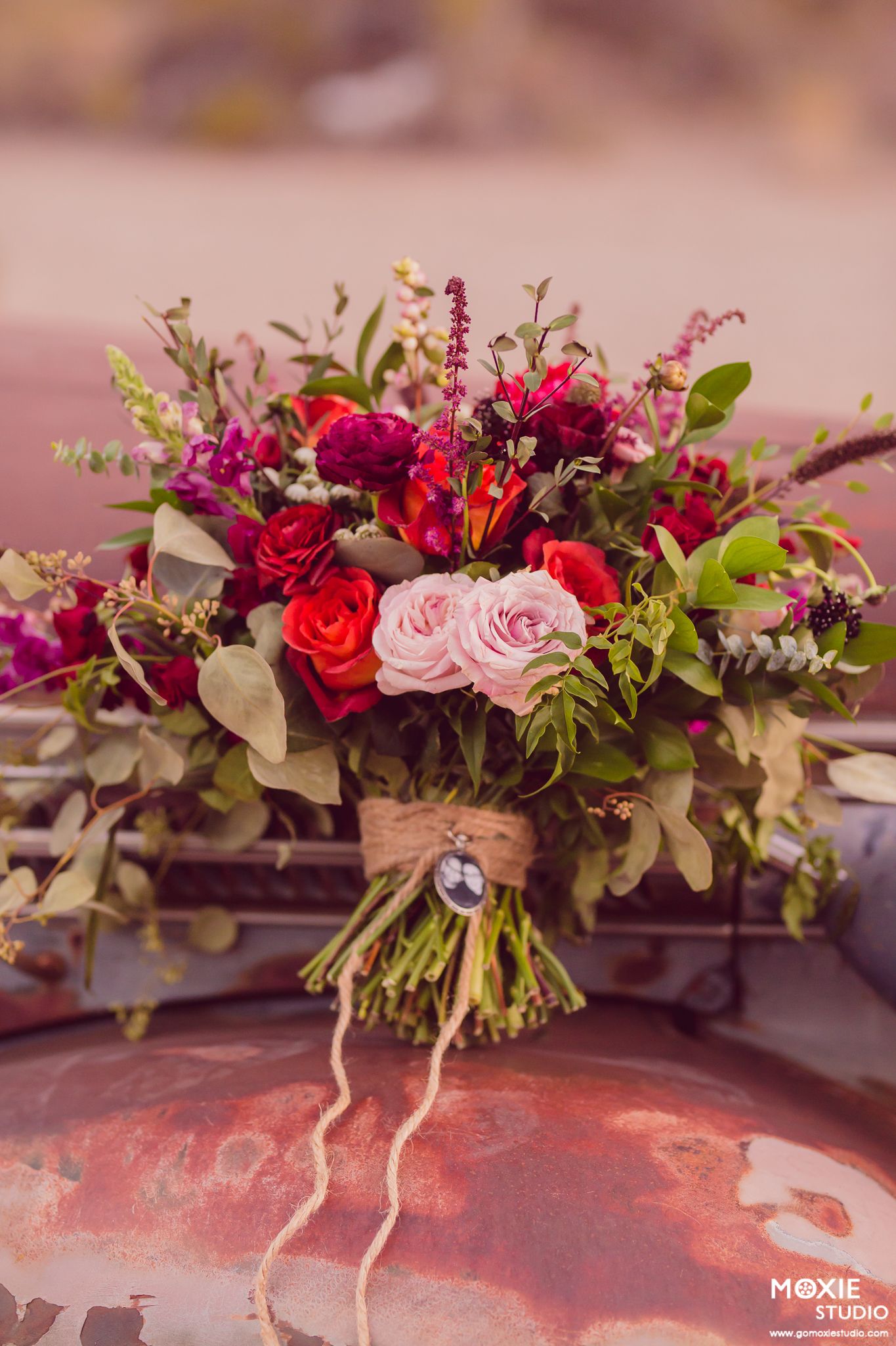 Elegant floral wedding bouquet featuring red and pink roses with greenery arranged in a romantic garden style.