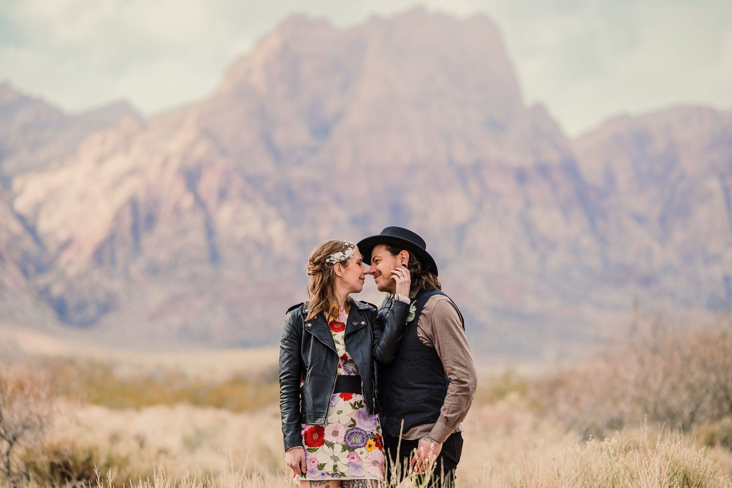 A couple shares an intimate moment in front of rugged mountain peaks during a desert photoshoot.
