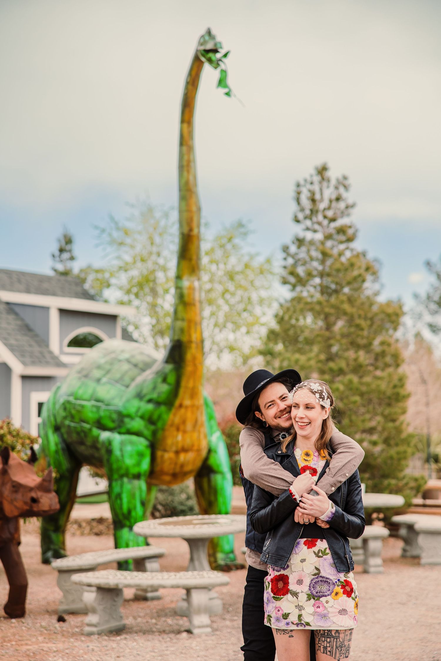 Large green dinosaur sculptures stand in a garden setting.